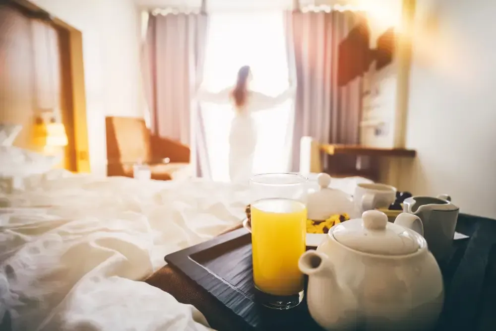 A tray of breakfast in a hotel room with a woman standing in the background.