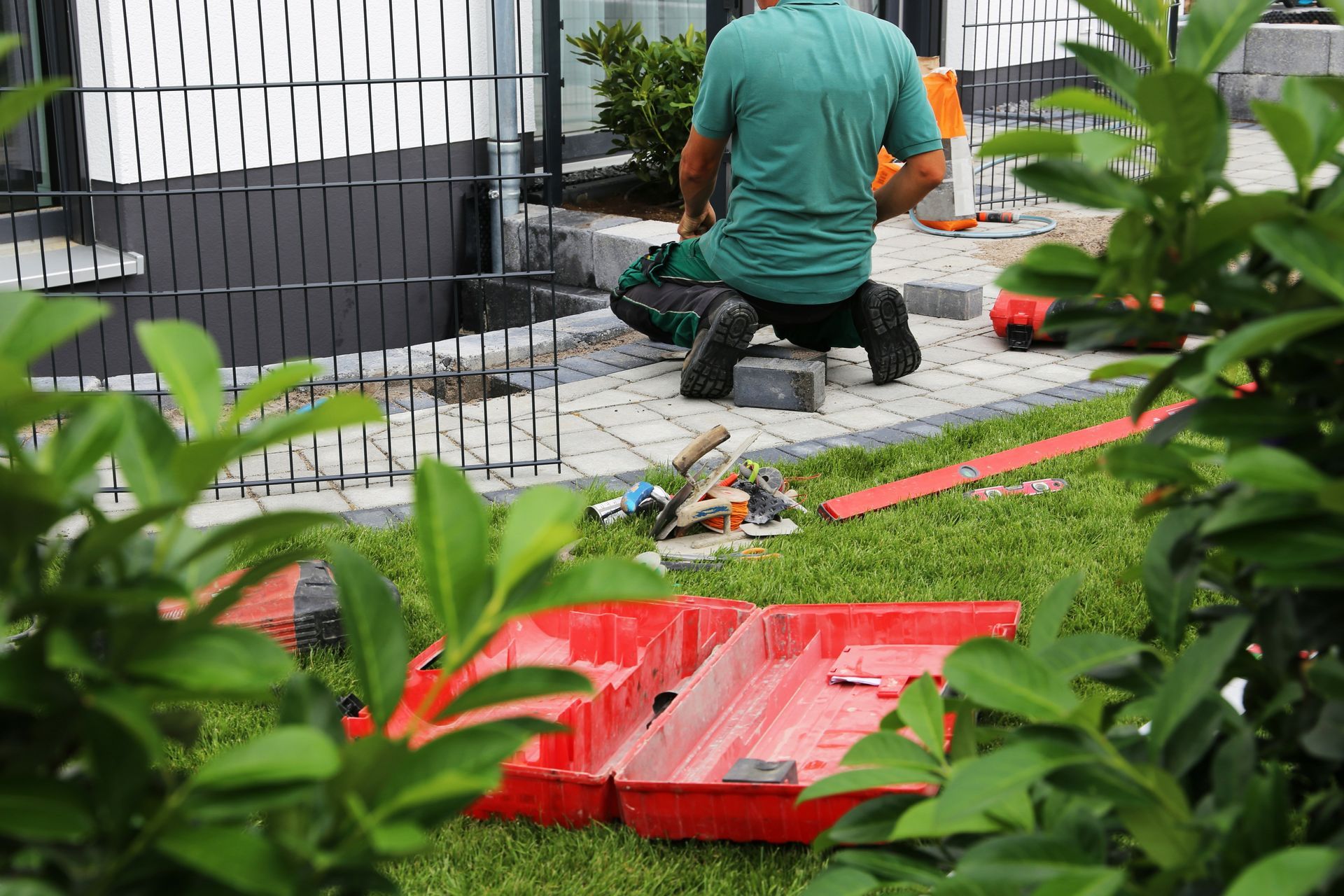 Ein Mann kniet im Gras, während er auf einer Terrasse arbeitet.
