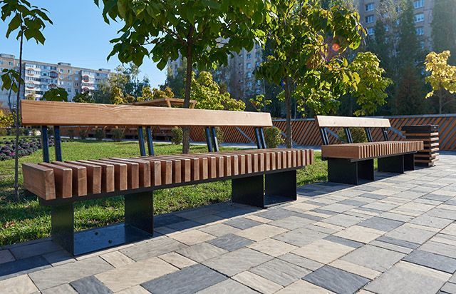Eine Reihe Holzbänke steht auf einem gepflasterten Gehweg in einem Park.