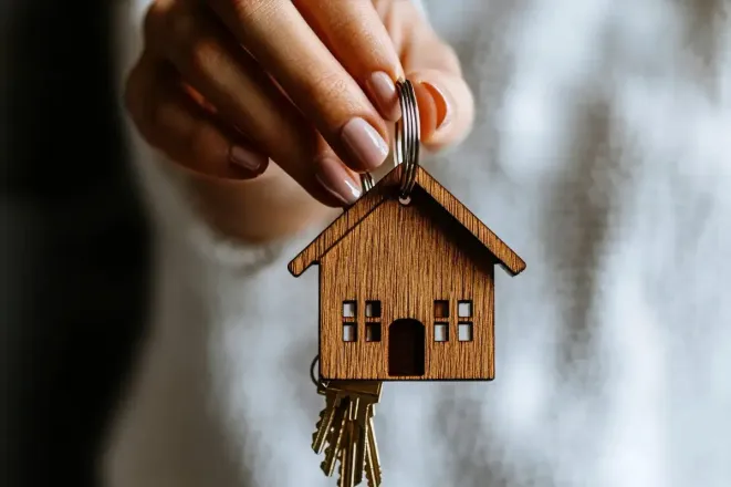 Mano sosteniendo un llavero con forma de casa con llaves, simbolizando la propiedad de la vivienda.