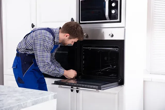 Un reparador con un mono azul examina el interior de un horno en una cocina.