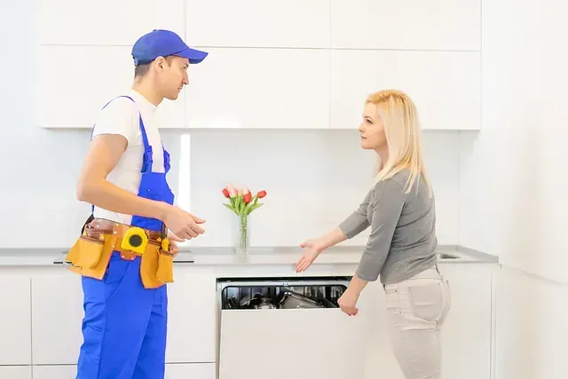 Un reparador con un mono azul y una mujer en una cocina, mirando un lavavajillas.