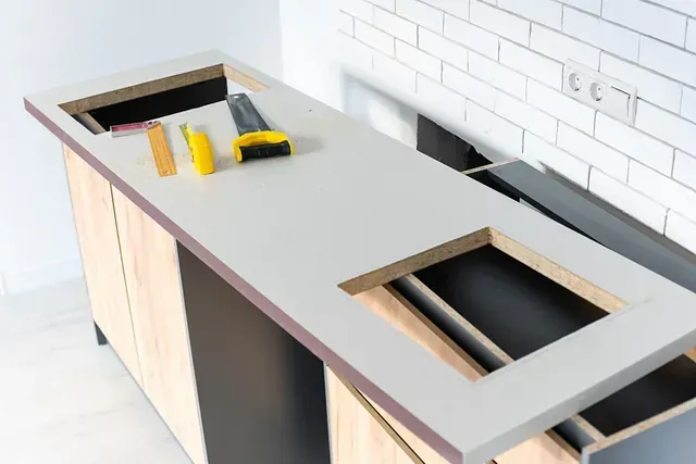 Instalación de encimera de cocina en progreso; beige con recortes para fregadero y estufa, herramientas presentes.
