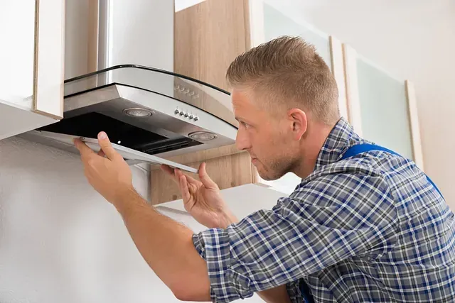 Hombre con camisa azul y a cuadros instalando una campana extractora de cocina, mirando atentamente.