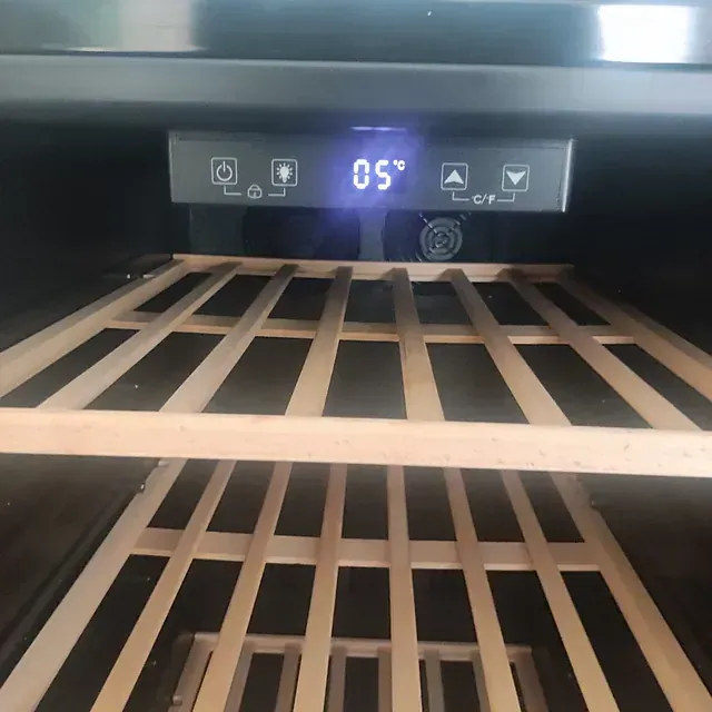 Interior de un enfriador de vinos con estantes de madera, pantalla digital de temperatura que muestra 5 ° C y panel de control.