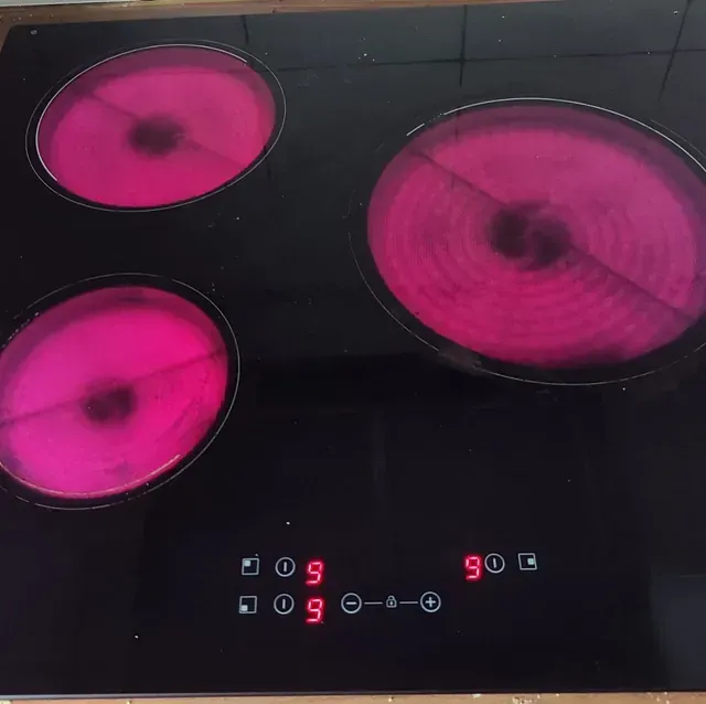 Estufa eléctrica negra con tres quemadores calientes de color rosa y controles digitales.