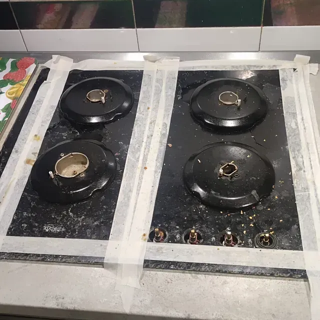 Estufa de color negro con cuatro quemadores, sellada con cinta para su limpieza.