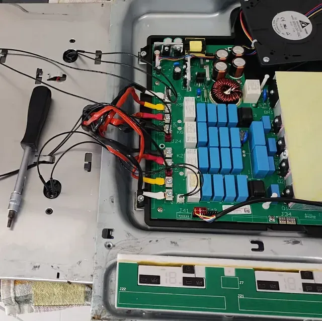 Placa de inducción abierta con placa de circuito, condensadores, ventilador y cableado; reparación en curso.
