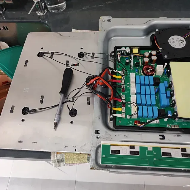 Placa de inducción abierta que revela componentes internos: placa de circuito, ventilador y fuente de alimentación.