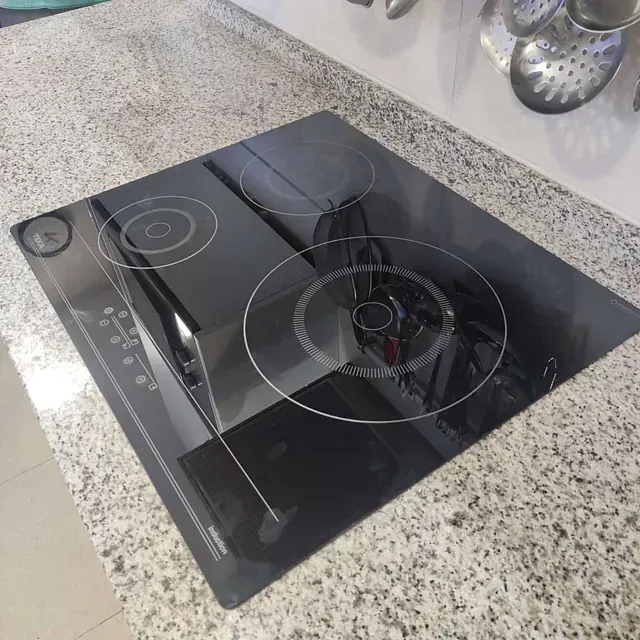 Estufa de vidrio negro con tres quemadores sobre una encimera de granito moteado.