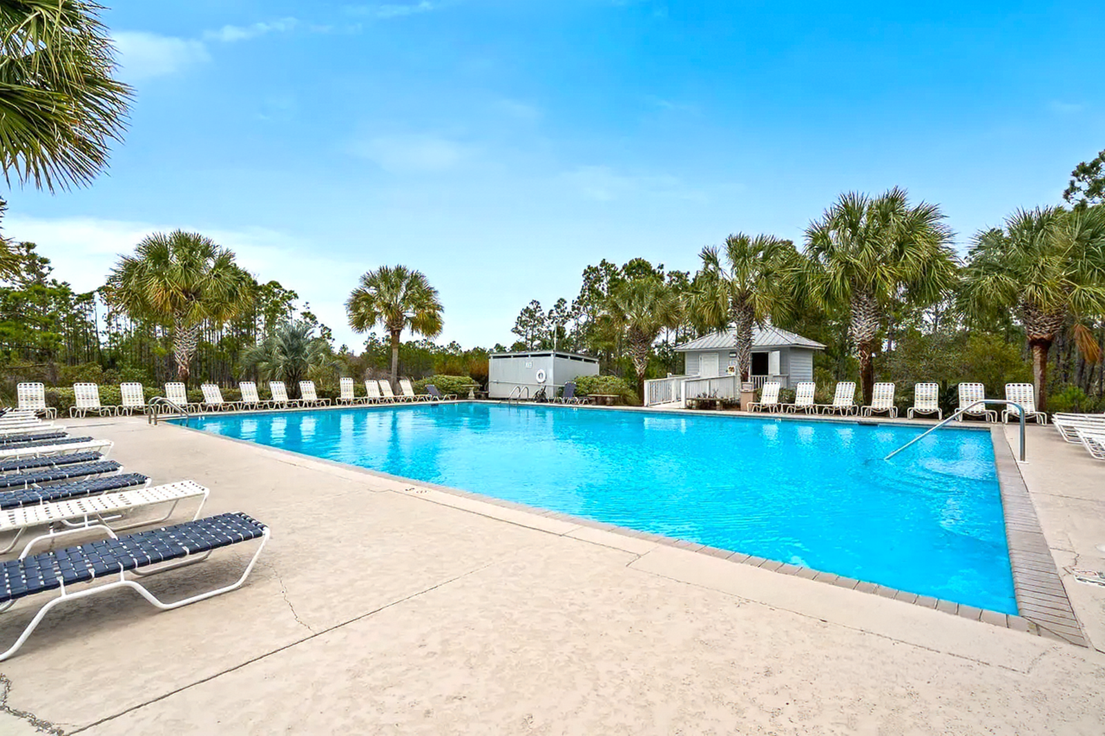 Outdoor swimming pool with lounge chairs, blue water, and a small pavilion under a clear sky