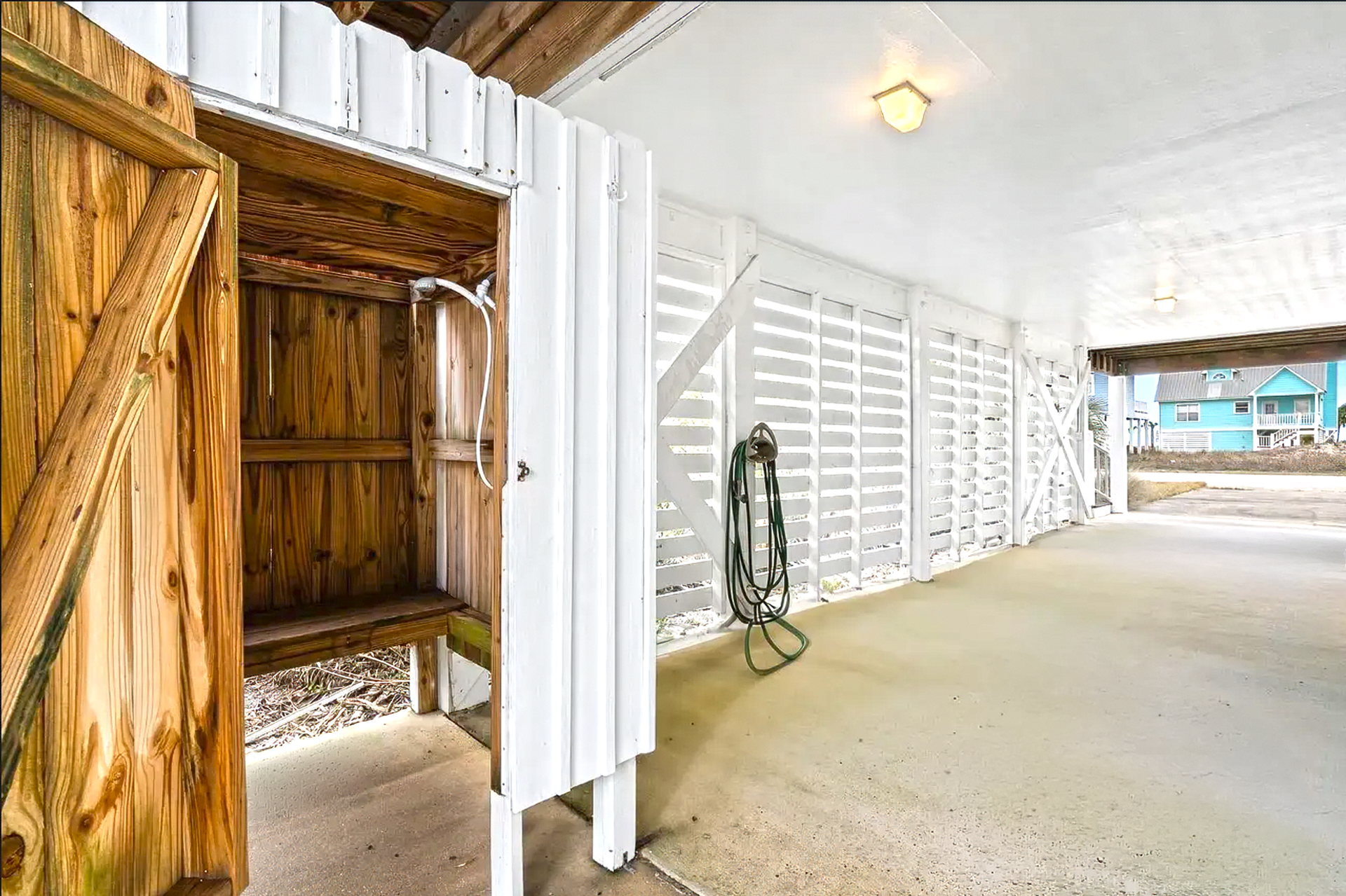 Covered patio with white lattice walls, concrete floor, and a wooden storage nook on the left
