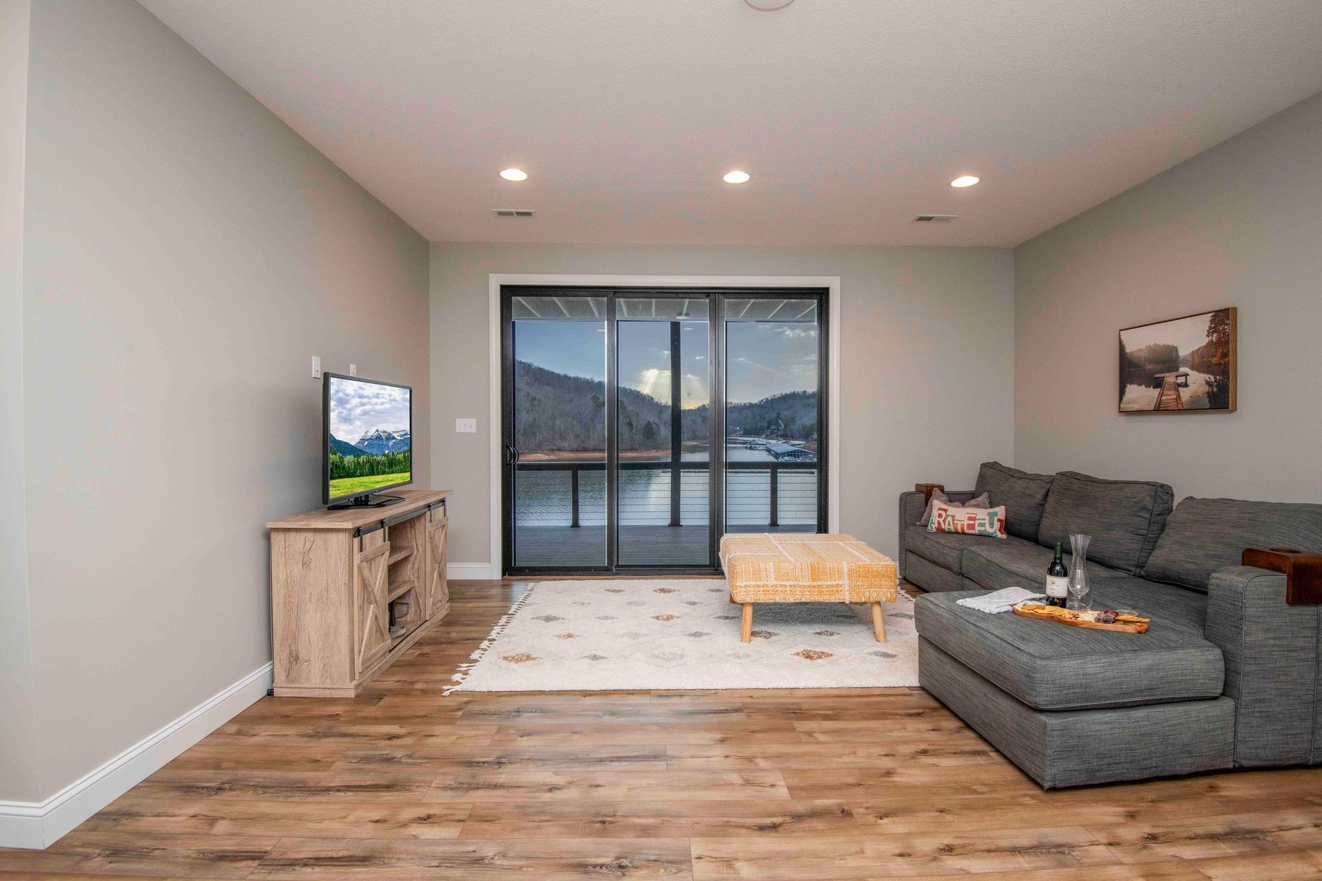 Living room with gray sectional, TV on wood console, and large glass doors overlooking water.
