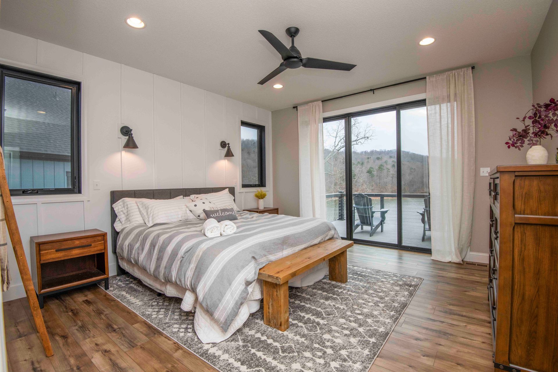 Bedroom with a large window overlooking a view, wooden bench at the foot of the bed, neutral colors.