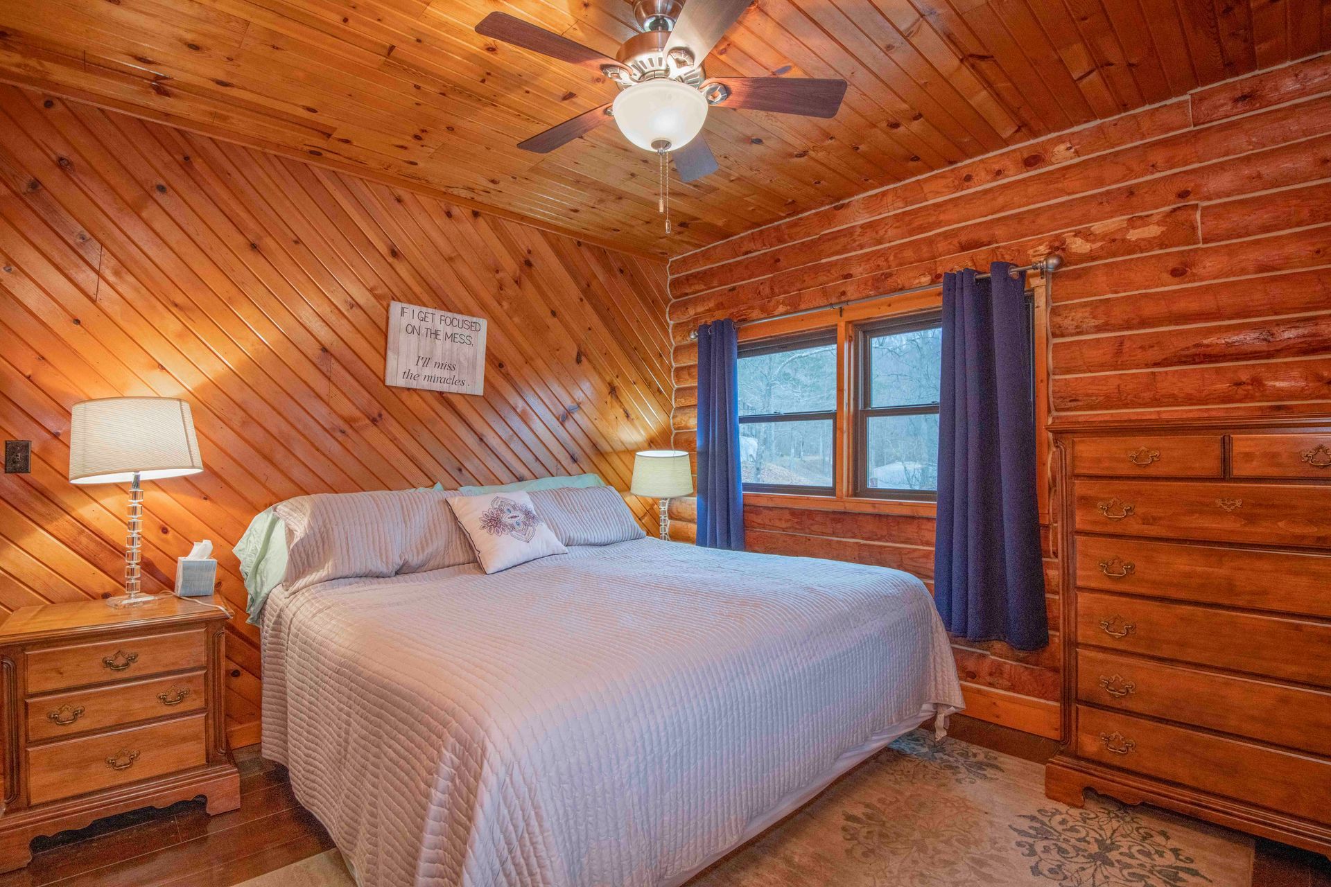 Bedroom with wood paneling, a bed with gray bedding, nightstands, and a dresser.