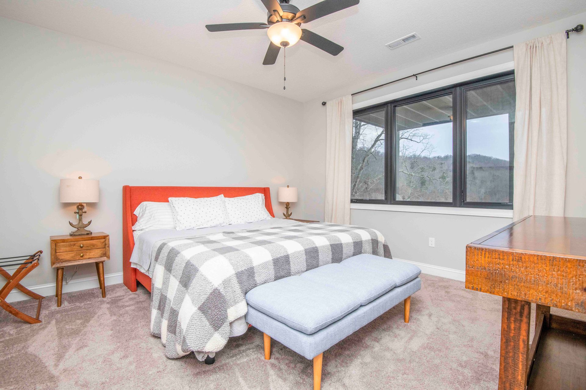 Bedroom with a bed, bench, nightstands, large window, and a desk. Gray walls and carpet.