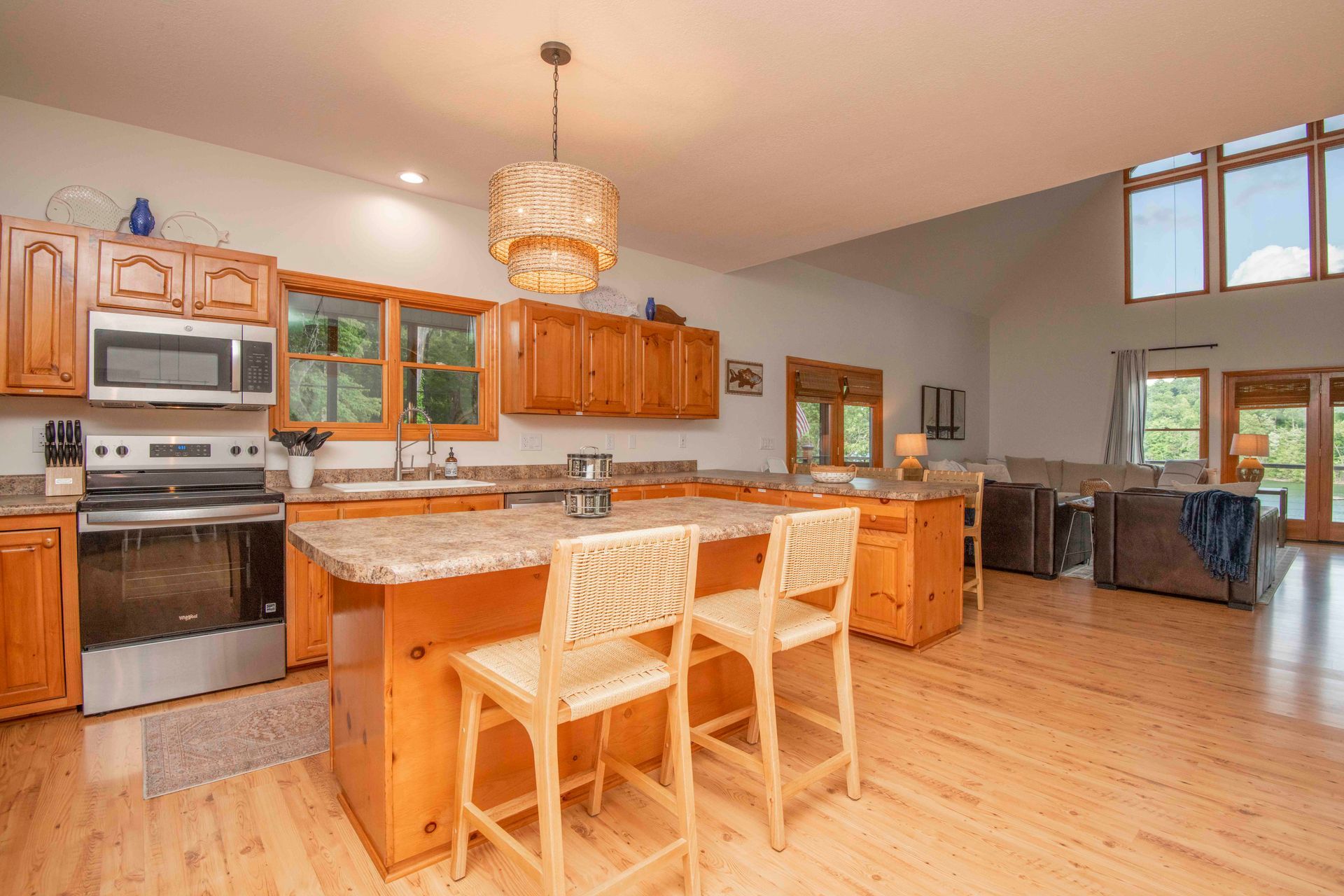 Kitchen with light wood cabinets, island with stools, and open to a living area.