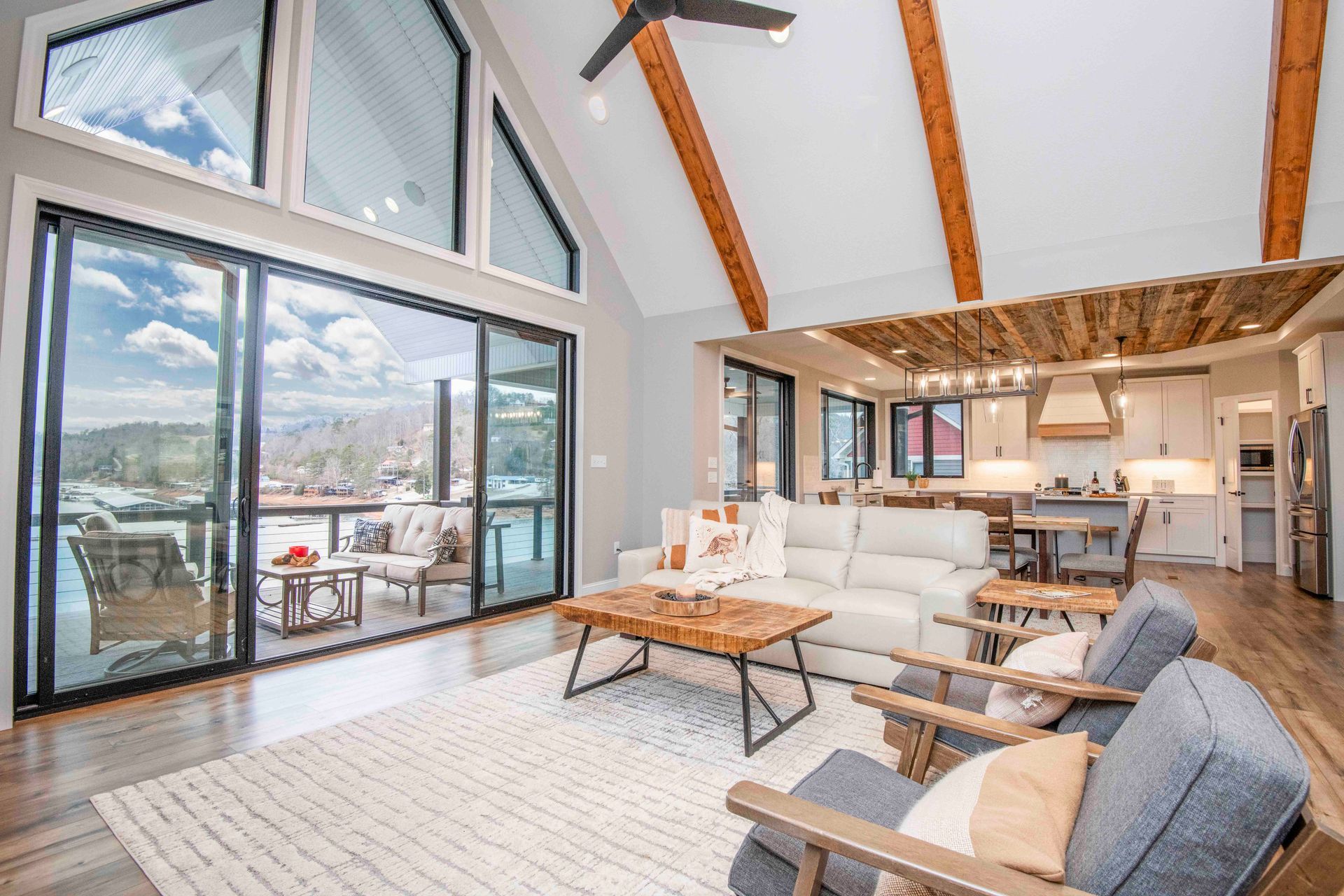 Living room with a sliding glass door, high ceilings, and wood beams, overlooking a scenic outdoor view.