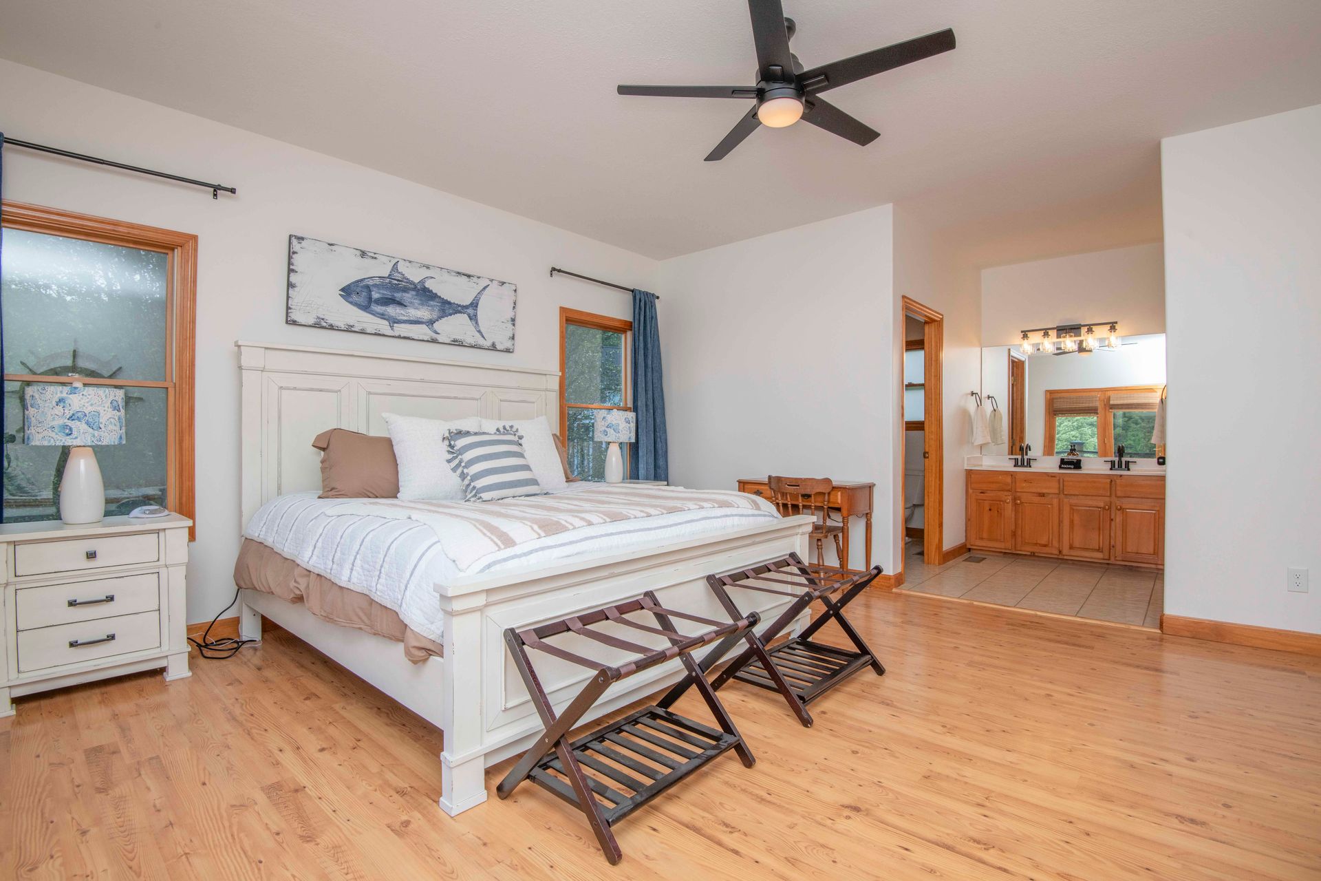 Bedroom with a white bed, wooden floor, and attached bathroom; nautical decor.