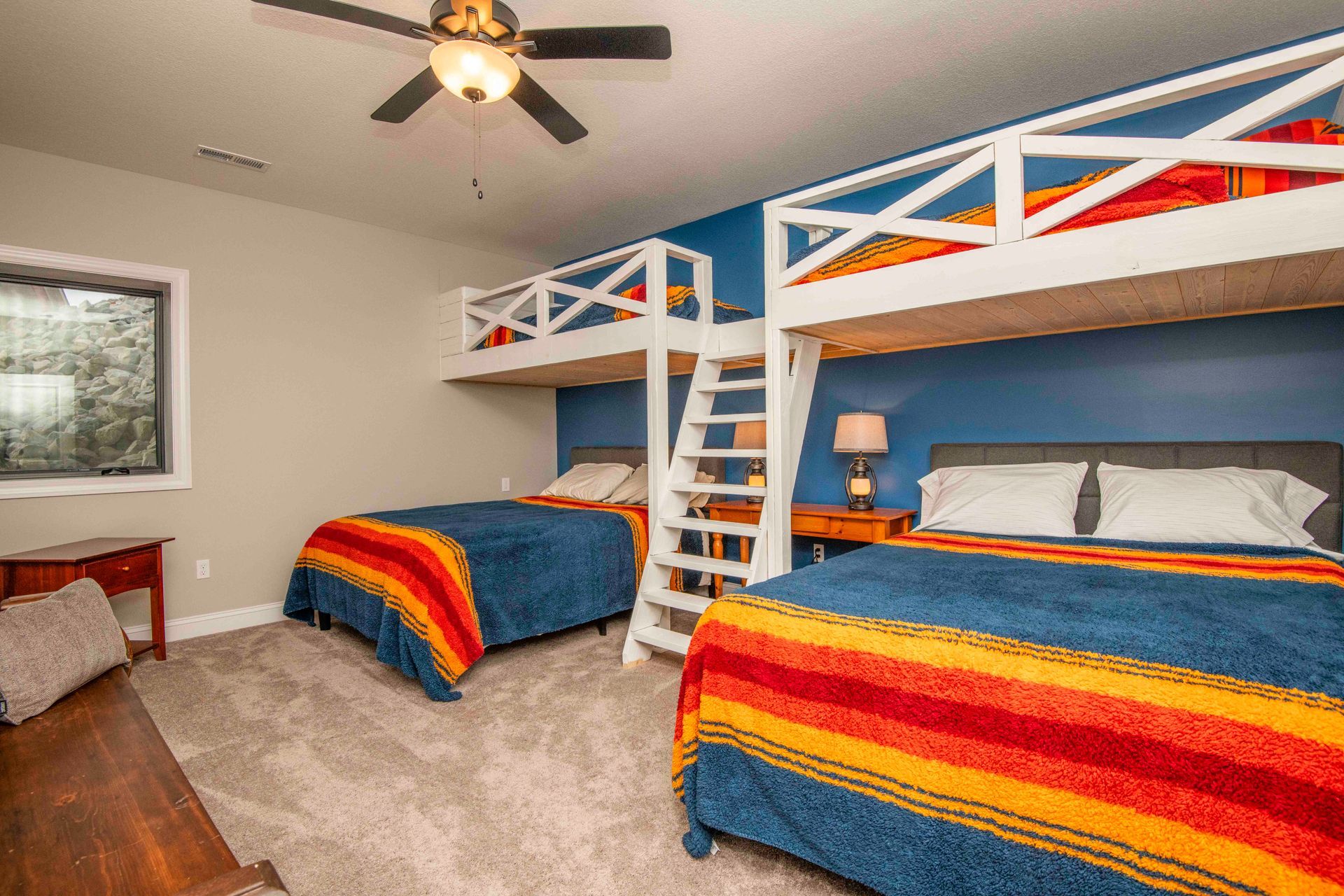 Bedroom with two beds, two bunk beds, blue and orange blankets, gray carpet, and blue wall.