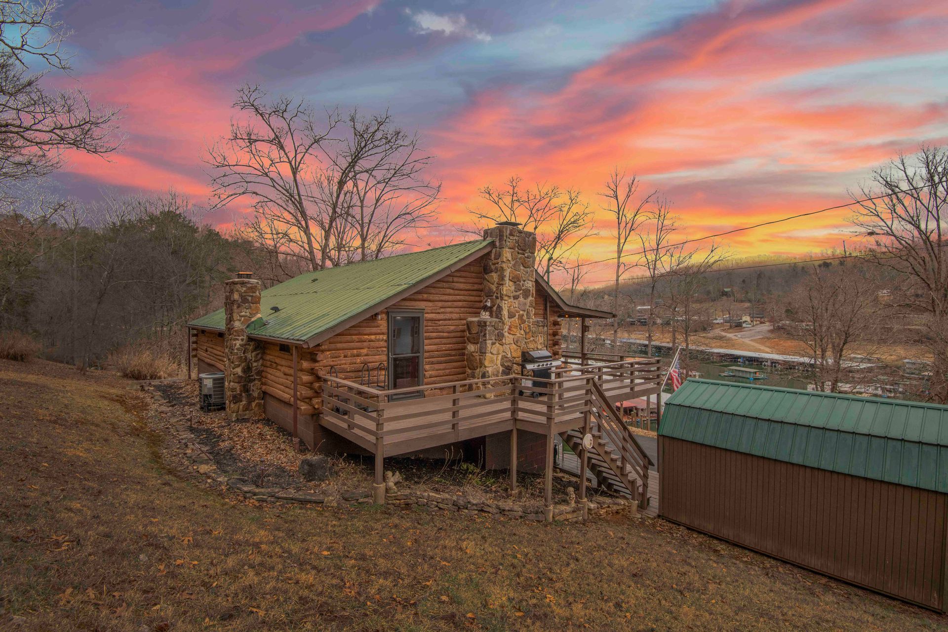 Log cabin with deck and stone chimney against a colorful sunset.