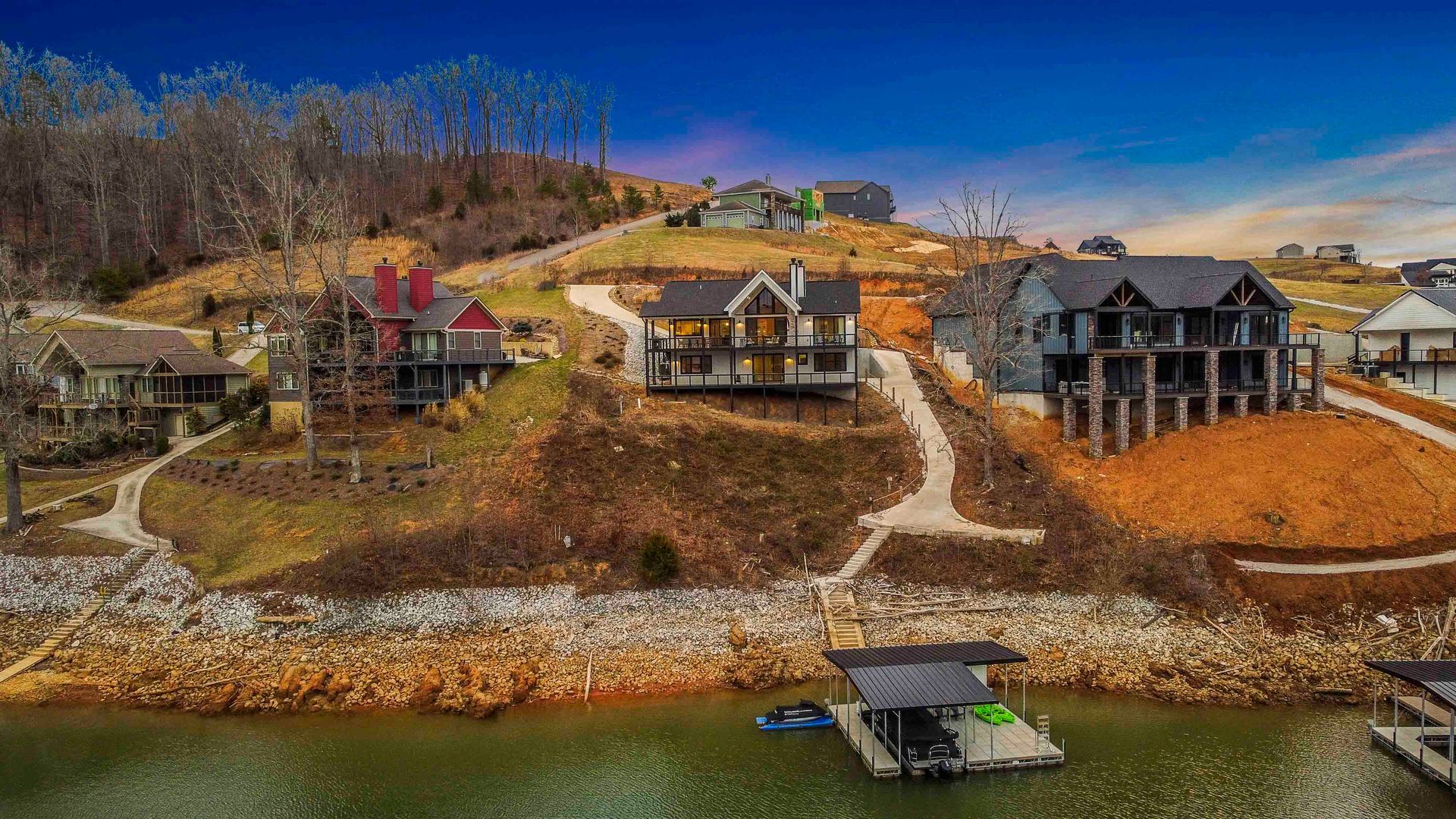 Houses on a hillside overlooking a lake, featuring docks and a clear blue sky.