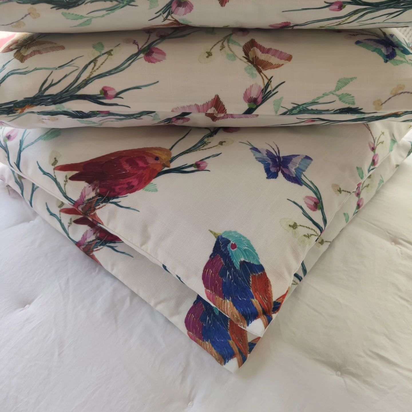 Una pila de almohadas con pájaros y flores sobre ellas.