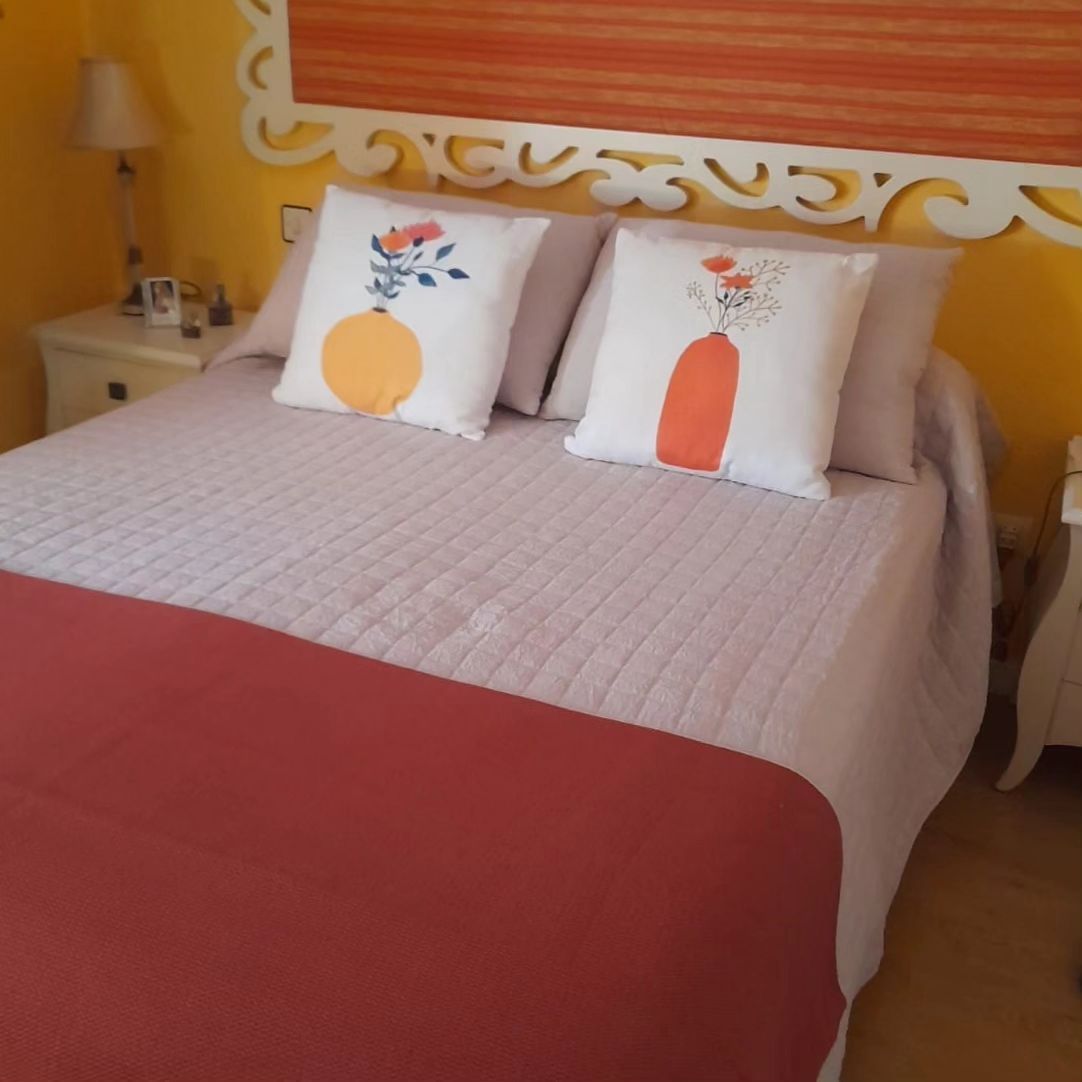 Una cama con almohadas y una pared amarilla detrás.