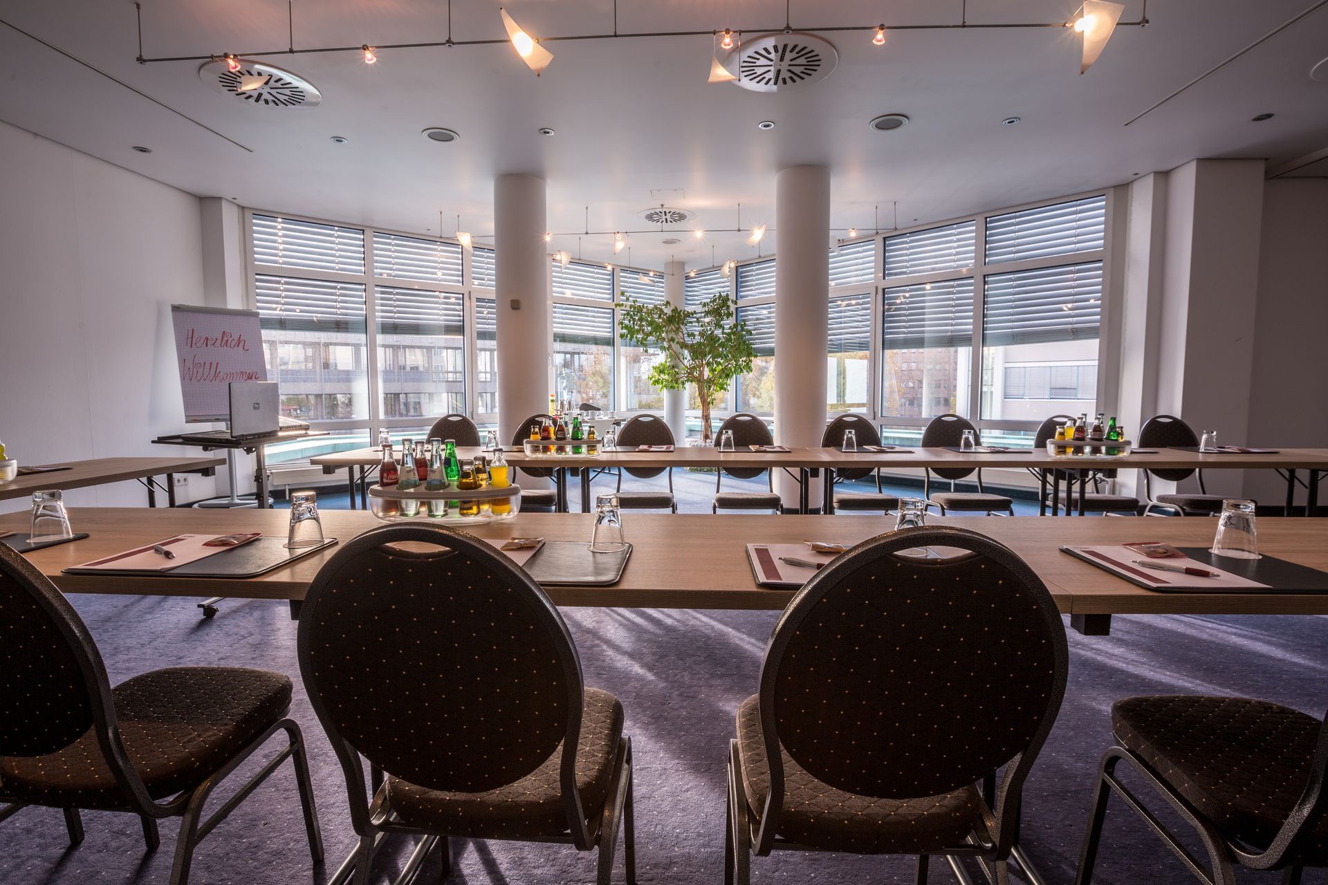 Moderner Konferenzraum mit geschwungenen Tischen, schwarzen Stühlen und großen Fenstern mit Blick ins Grüne