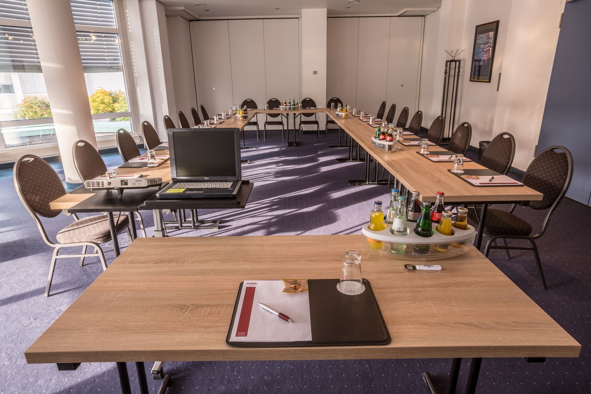 Konferenzraum mit langen Tischen, Stühlen, einem Laptop und Notizbüchern, ausgestattet für ein Meeting