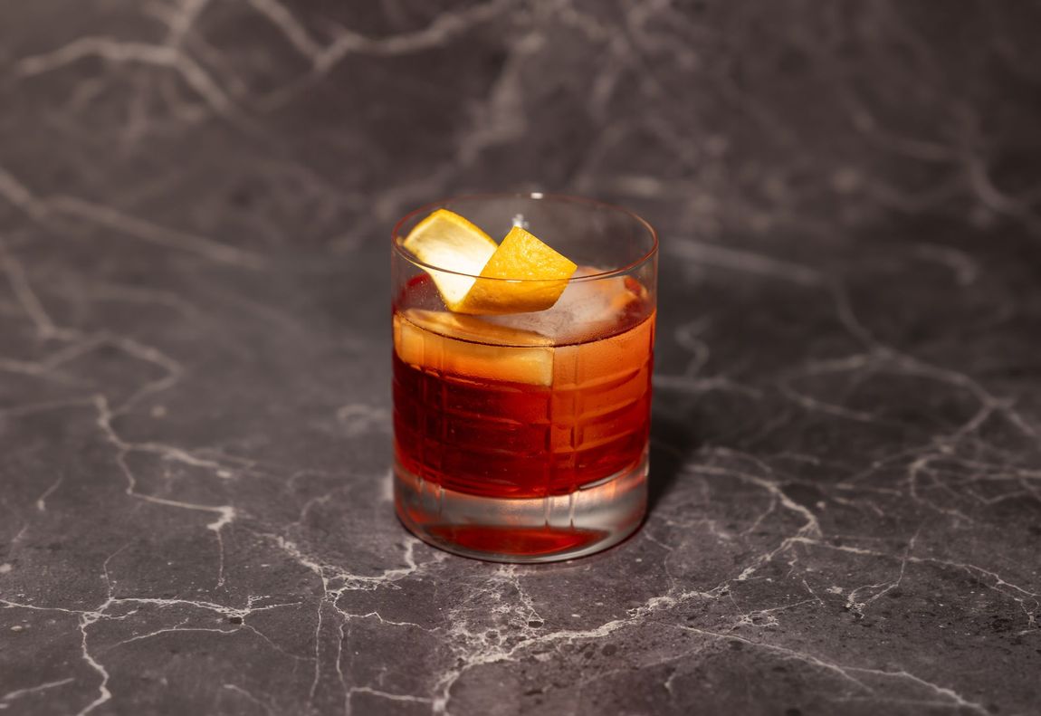 Bernsteinfarbener Cocktail in einem kurzen Glas mit Orangenschalengarnitur auf einer dunklen Marmoroberfläche