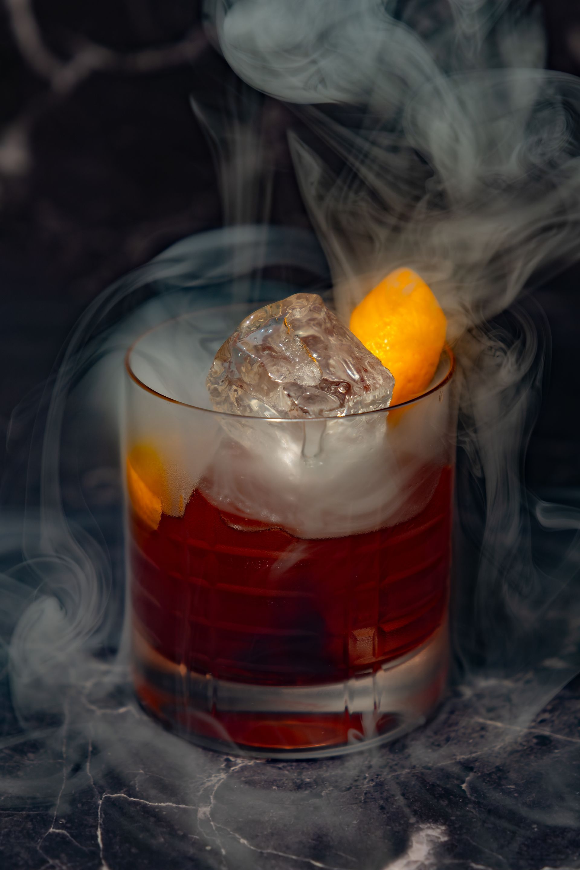 Rauchig-roter Cocktail in einem Tumbler mit Eis und einer Orangenscheibe als Garnitur