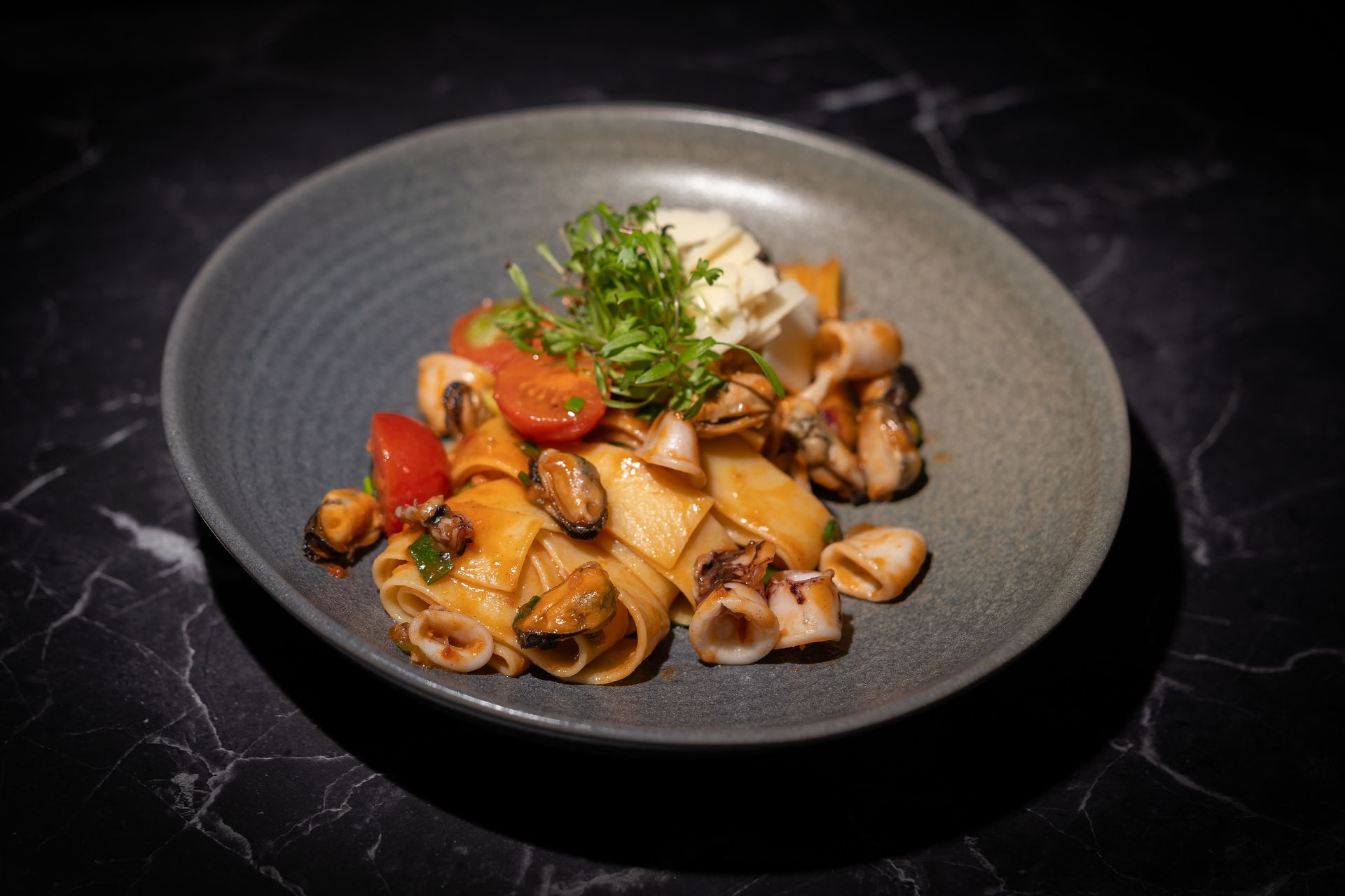 Pasta mit Champignons und Kirschtomaten auf einem grauen Teller, garniert mit frischen Kräutern