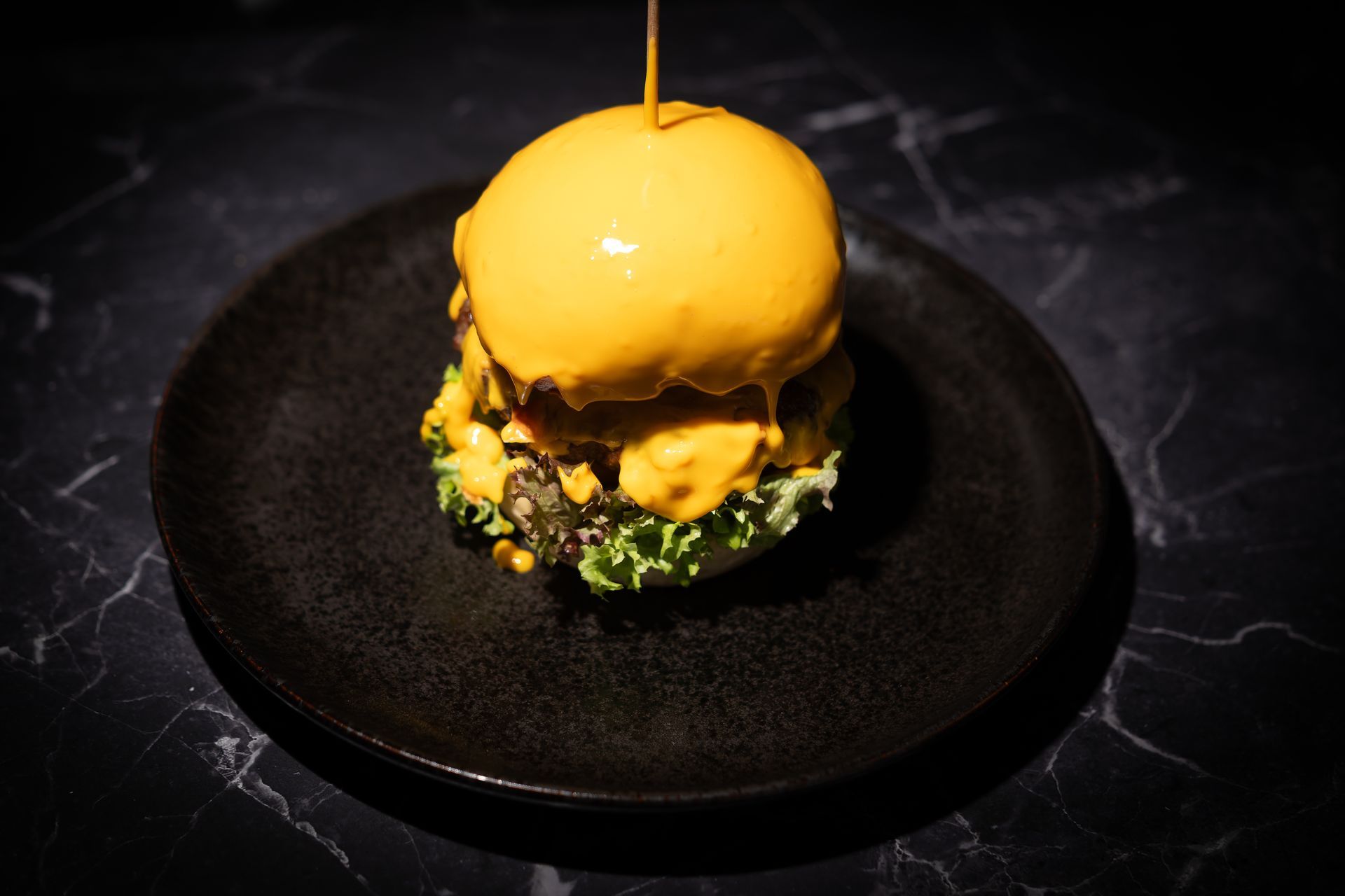 Gourmet-Burger mit glänzend gelbem Brötchen auf einem schwarzen Teller, garniert mit Grünzeug auf einer dunklen Tischplatte