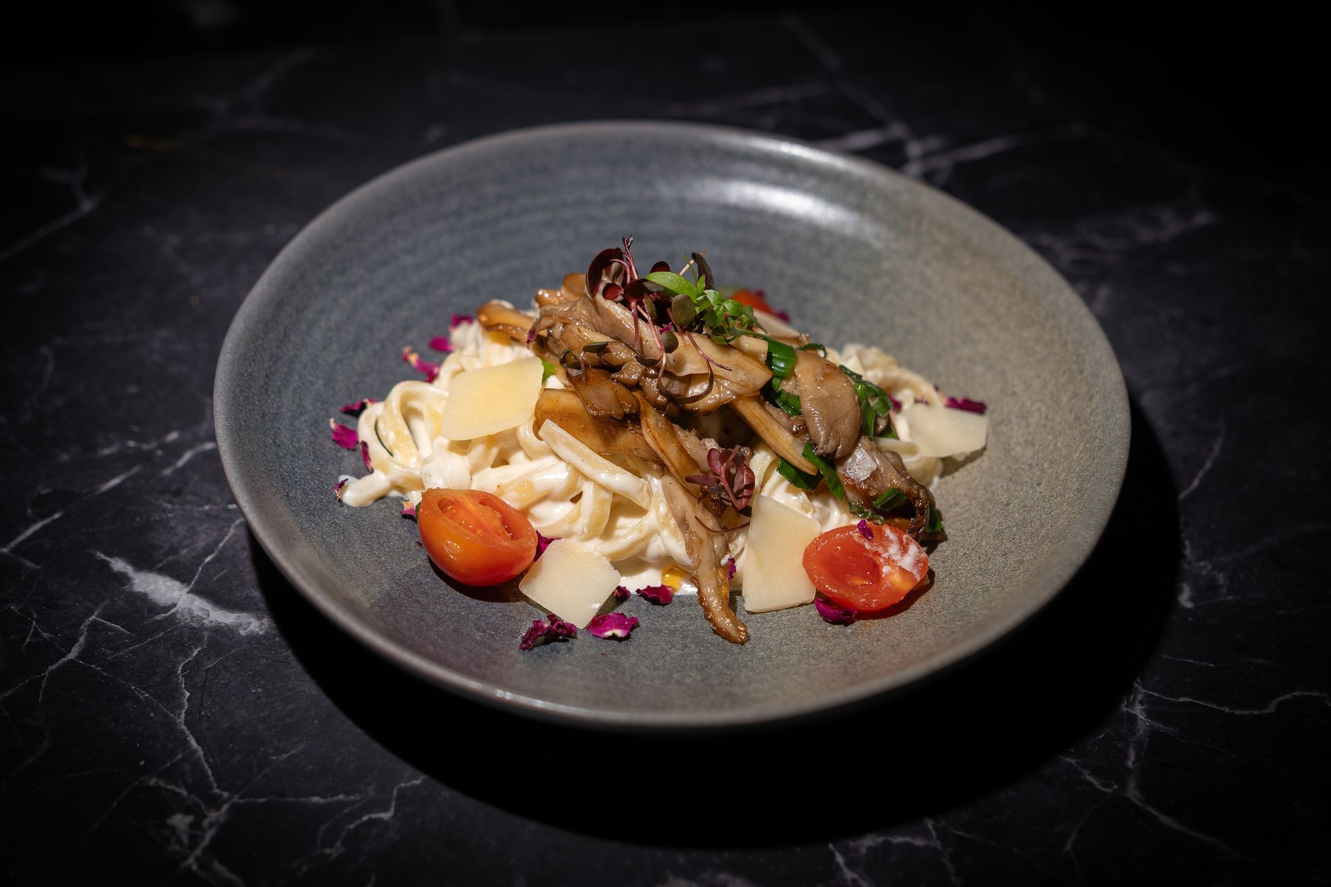 Ein auf einem grauen Teller angerichtetes Gourmetgericht mit geschnittenem Fleisch, cremiger Soße, Erdbeeren und violetter Garnierung.