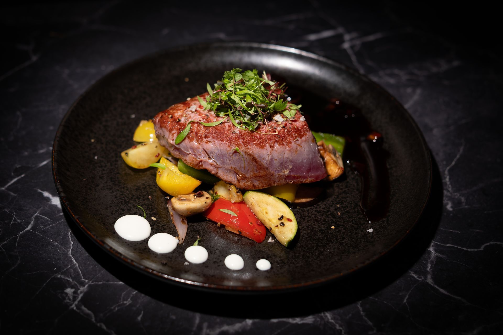 In der Pfanne gebratenes Steak mit Kartoffeln und Sauce auf einem schwarzen Teller, garniert mit Kräutern