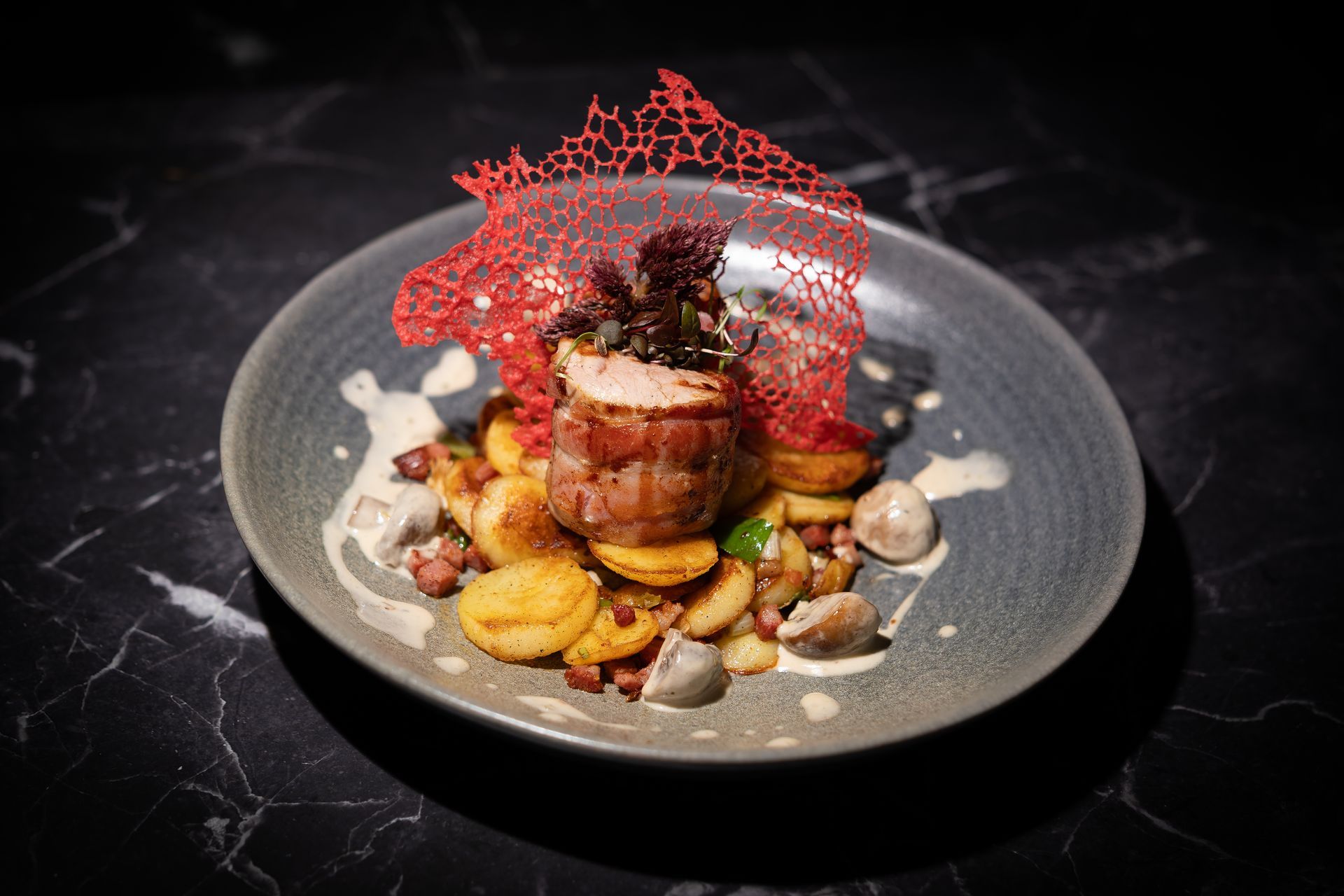 Gourmet-Gericht mit angebratenem Fleisch, Gemüse und roter Zuckergarnitur auf einem grauen Teller