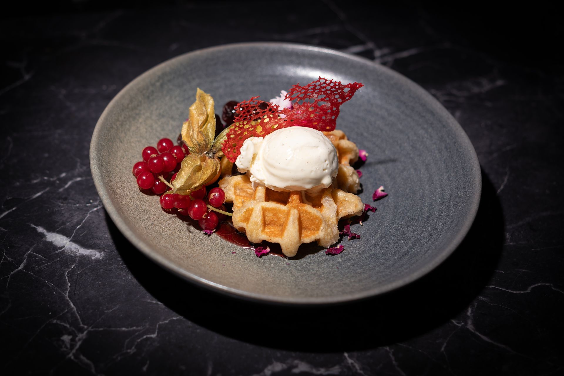 Waffeldessert mit Vanilleeis, Beeren und roter Soße auf einem dunklen Teller