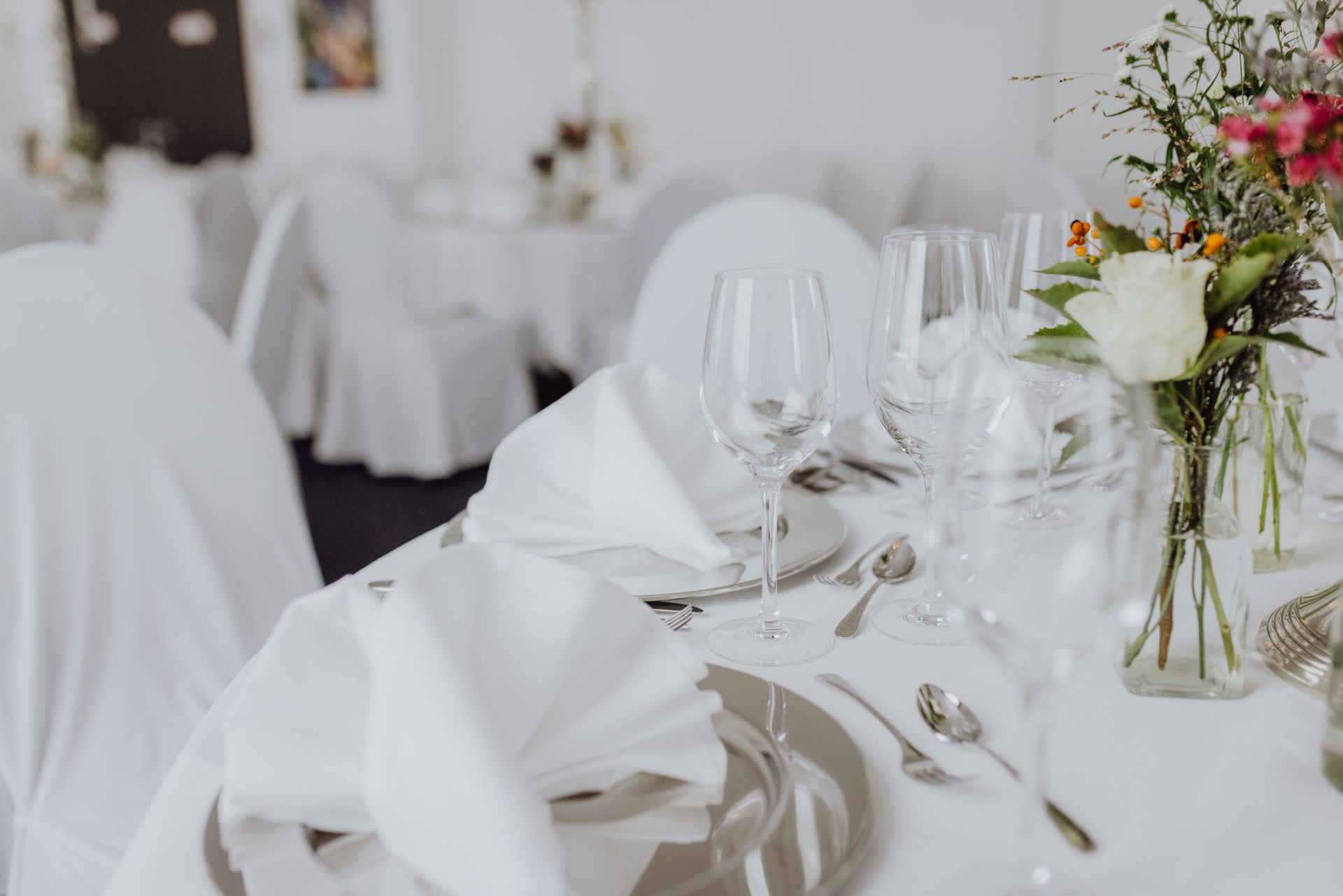 Elegant gedeckter, weiß gedeckter Banketttisch mit gefalteten Servietten, Gläsern und Blumengestecken.