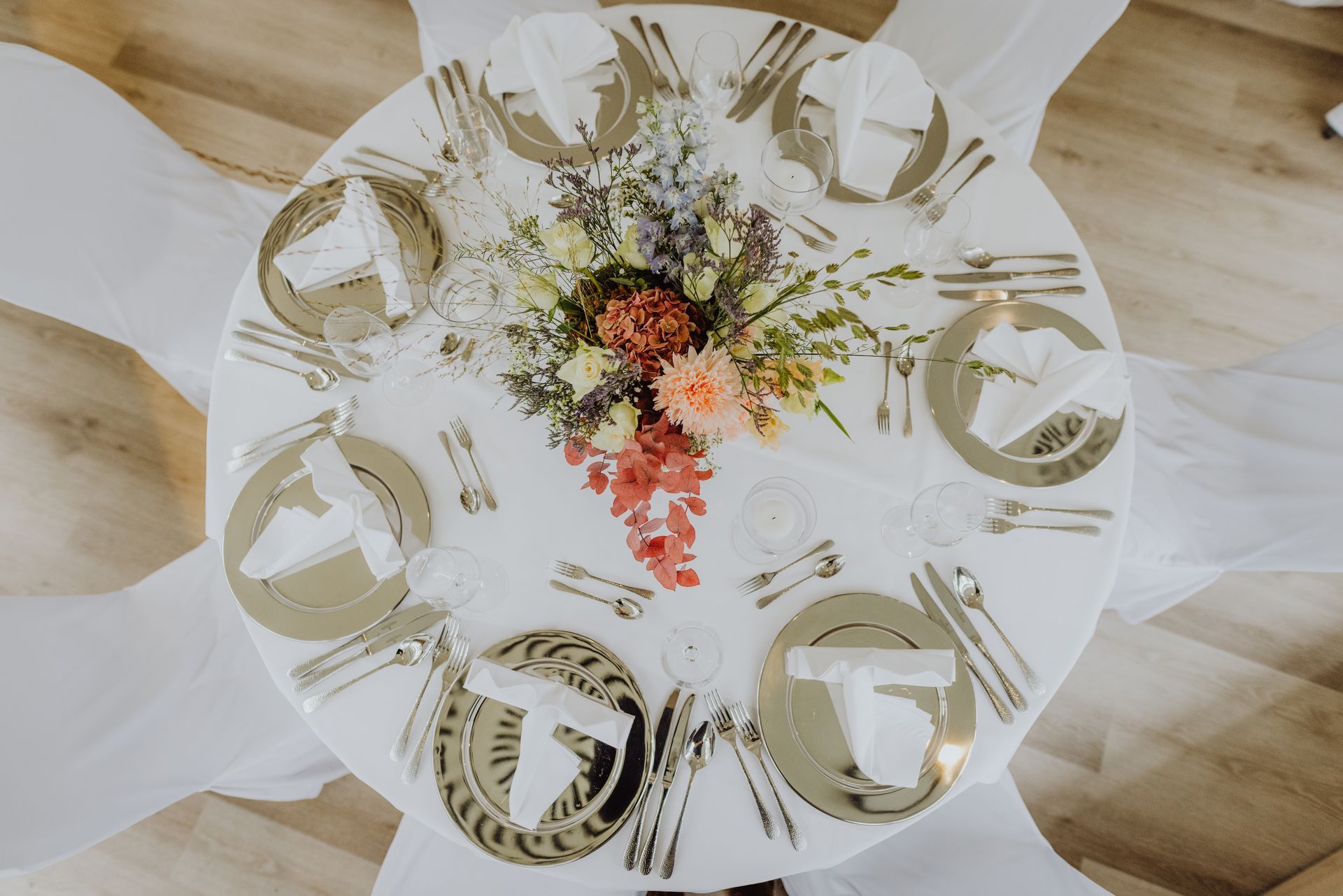 Runder weißer Tisch mit sechs Stühlen und einem kleinen Blumenarrangement auf einem Holzboden.