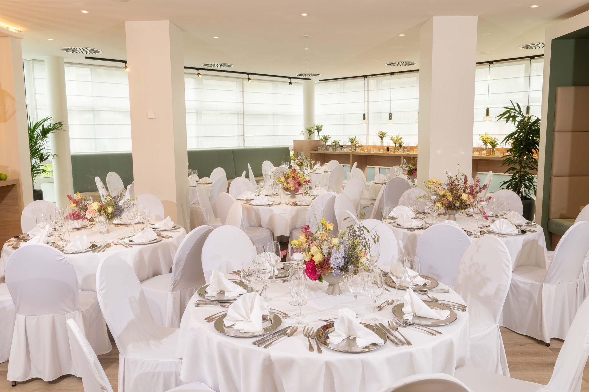 Eleganter weißer Festsaal, ausgestattet für eine formelle Veranstaltung mit runden Tischen, Stühlen und floralen Tischdekorationen.