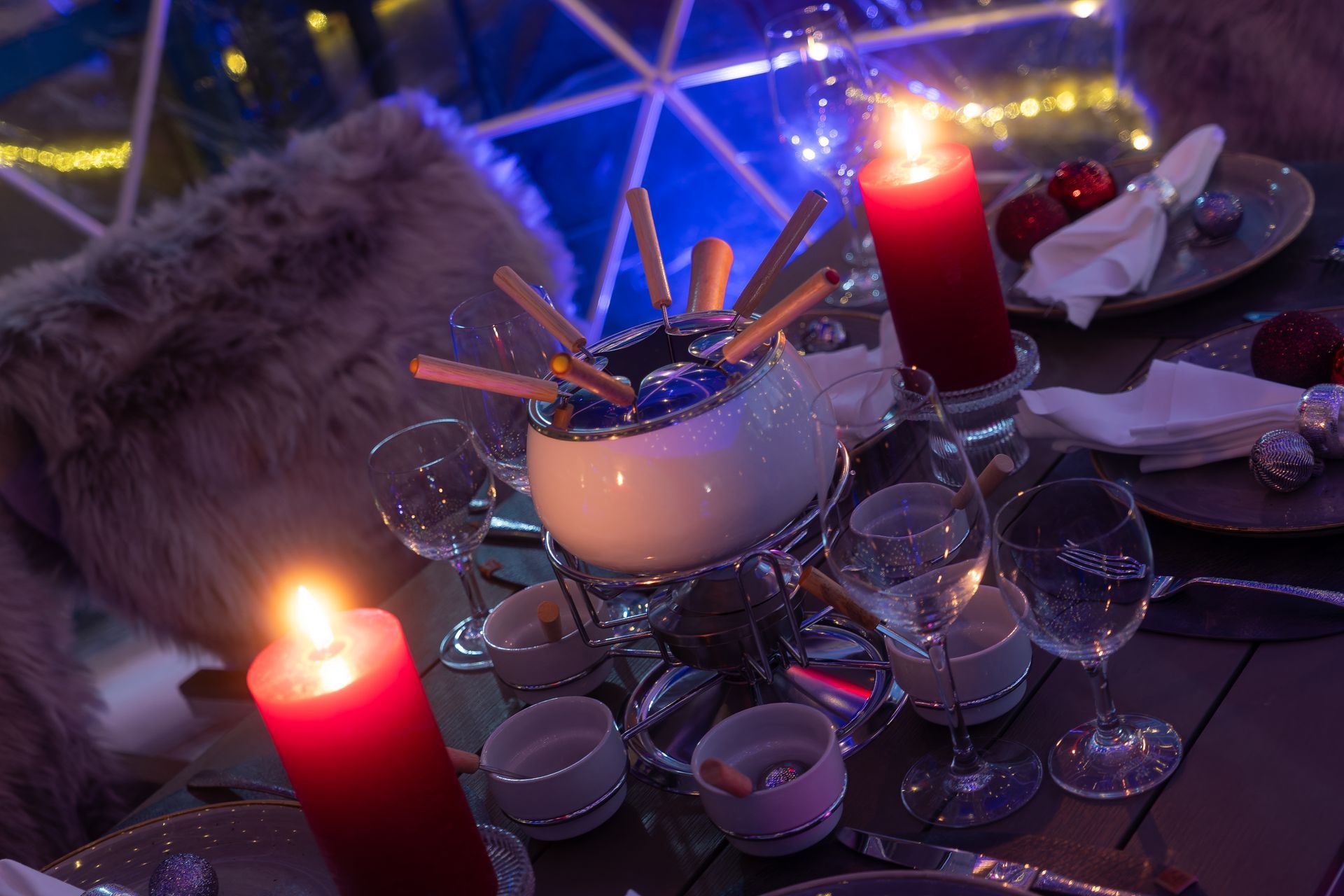 Ein mit Kerzen beleuchteter Partytisch mit einer gläsernen Bowleschüssel, Bechern, Tellern und einem daneben drapierten Pelzmantel.