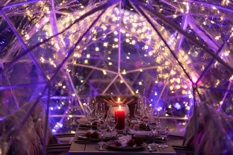 Ein gedeckter Tisch im Kerzenschein in einer leuchtend violetten geodätischen Kuppel mit Lichterketten und funkelnder Dekoration