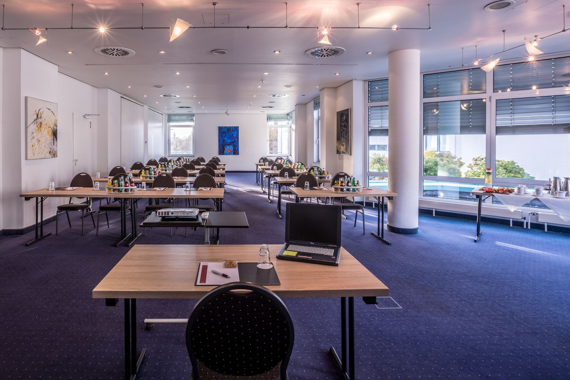 Moderner Bürobesprechungsraum mit langen Tischen, Stühlen und großen Fenstern mit Blick ins Grüne
