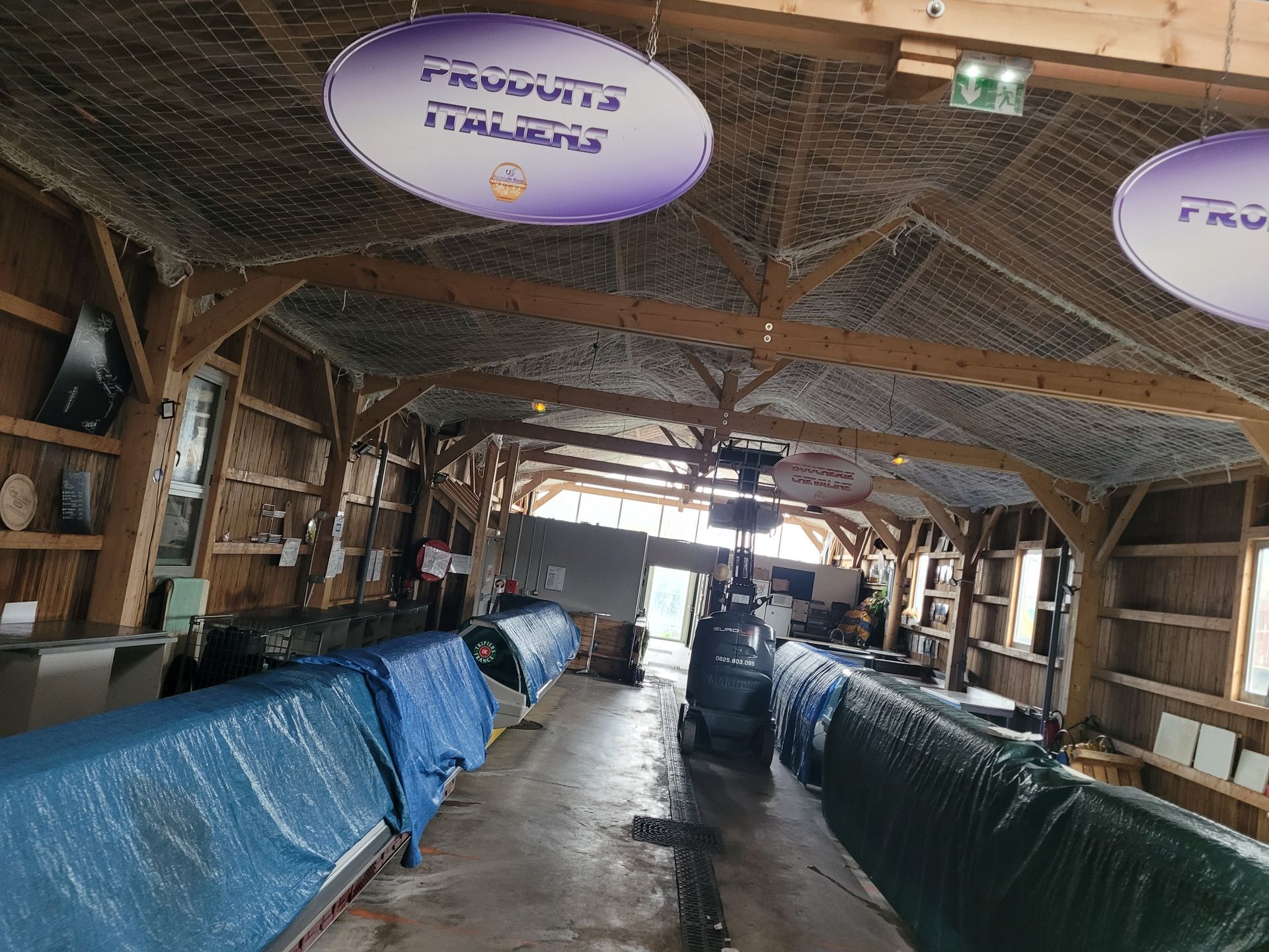 Marché avec des poutres en bois et des objets recouverts de bâches avec un filet anti-volatiles.