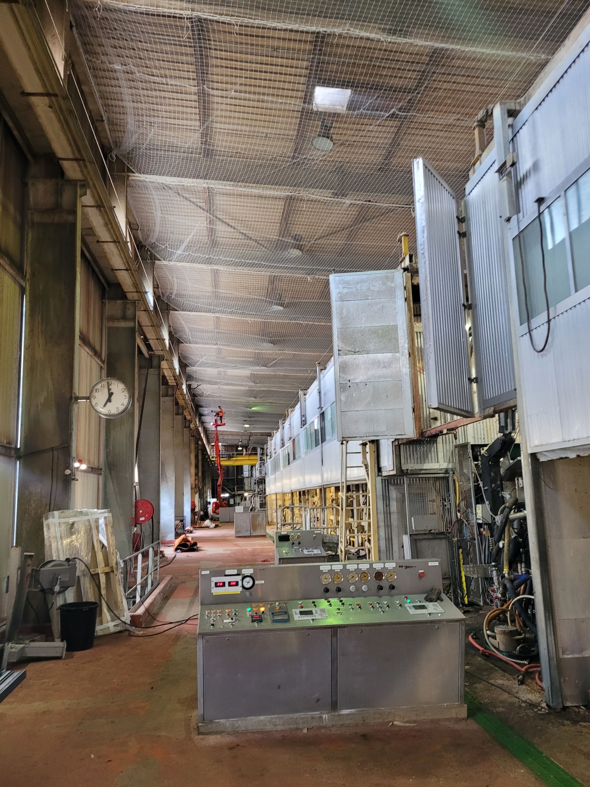 Intérieur industriel avec panneau de commande et machines le long d'un couloir. Filets de sécurité au plafond.