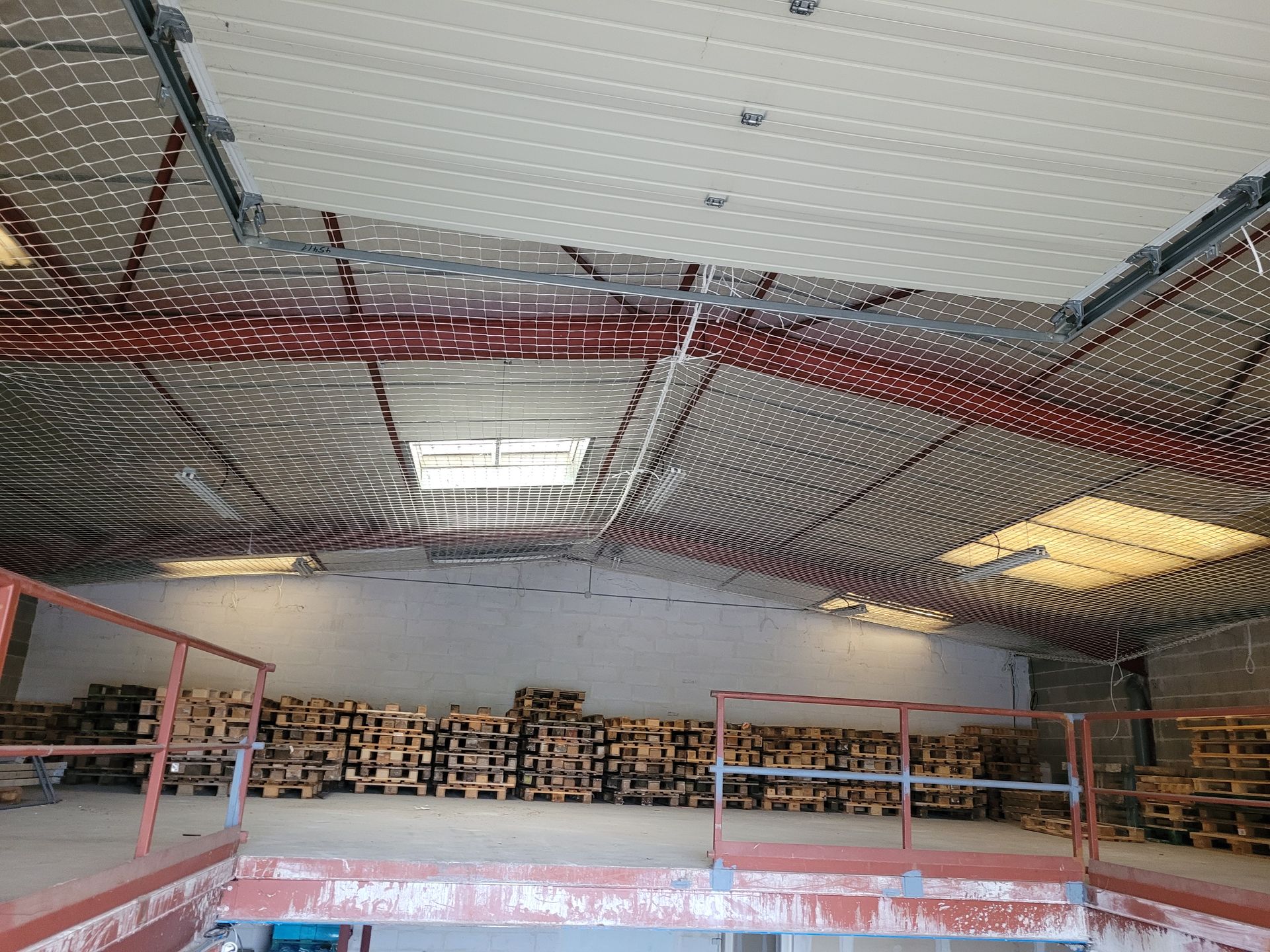 Intérieur d'un entrepôt avec filets de sécurité installés sous le plafond et au-dessus des puits de lumière.