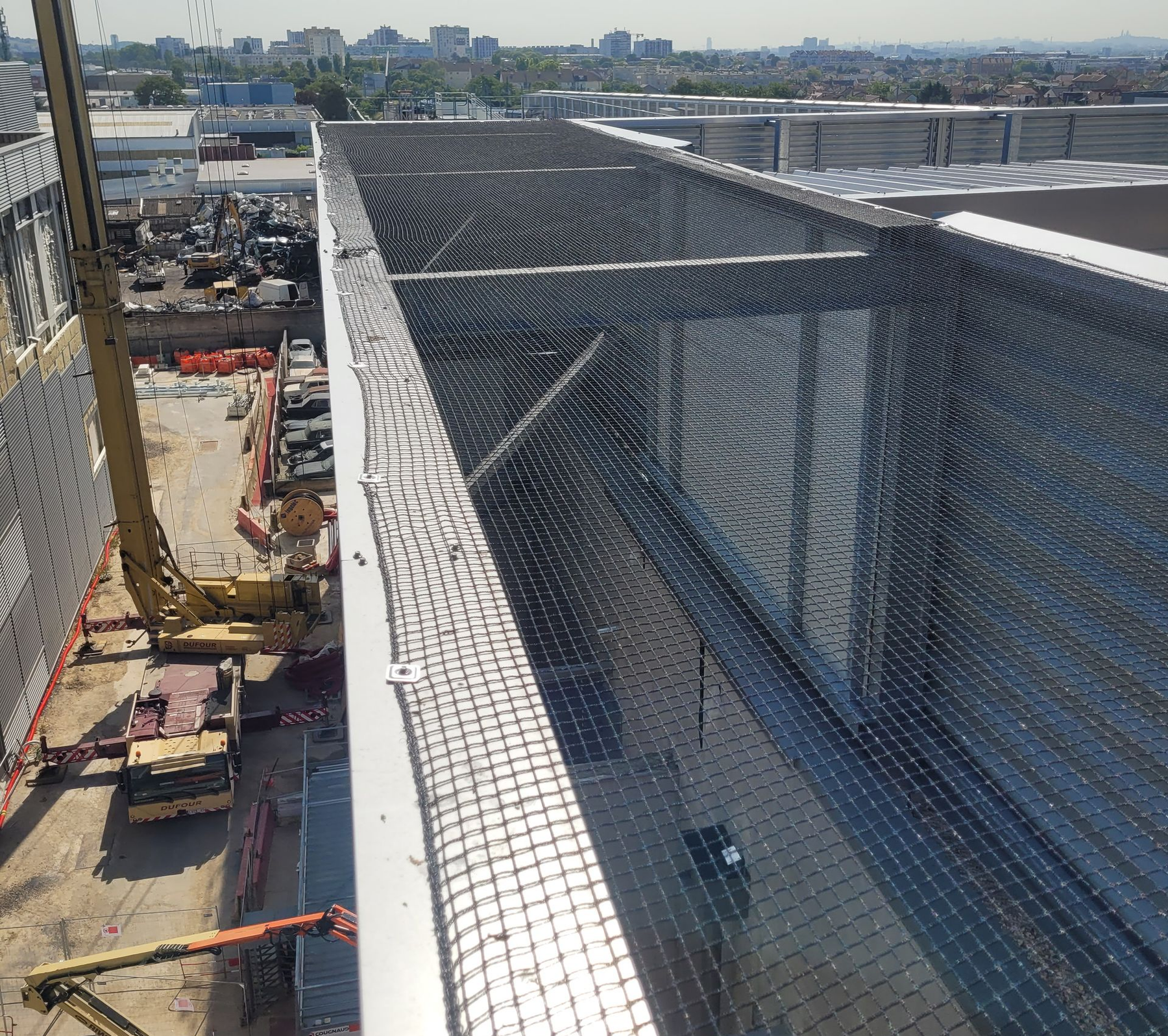 Chantier de construction avec filet de sécurité installé en bordure du bâtiment ; grue et autres équipements visibles.