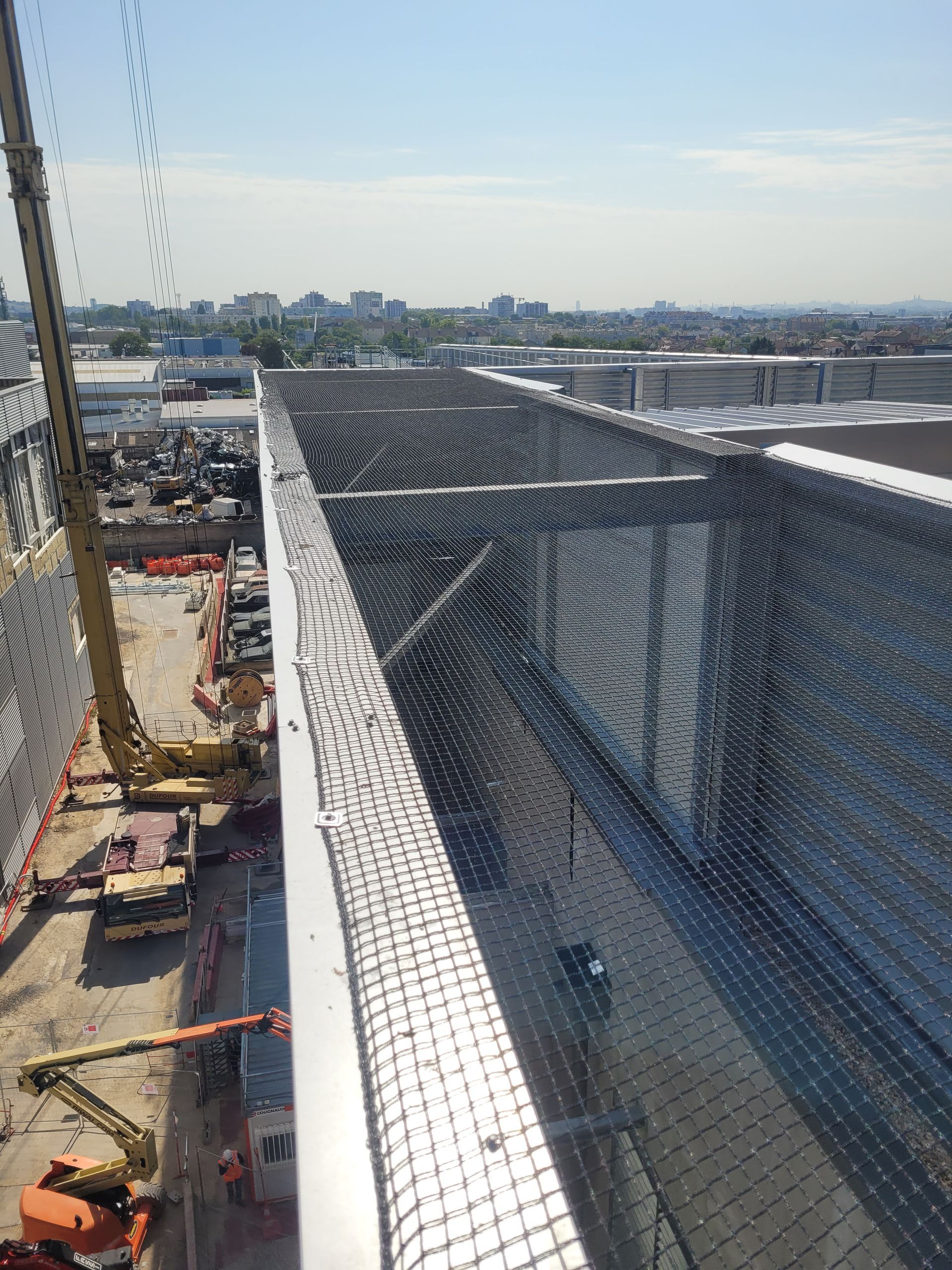 Vue d'un chantier de construction : structure métallique, filet de sécurité, grue, machines.
