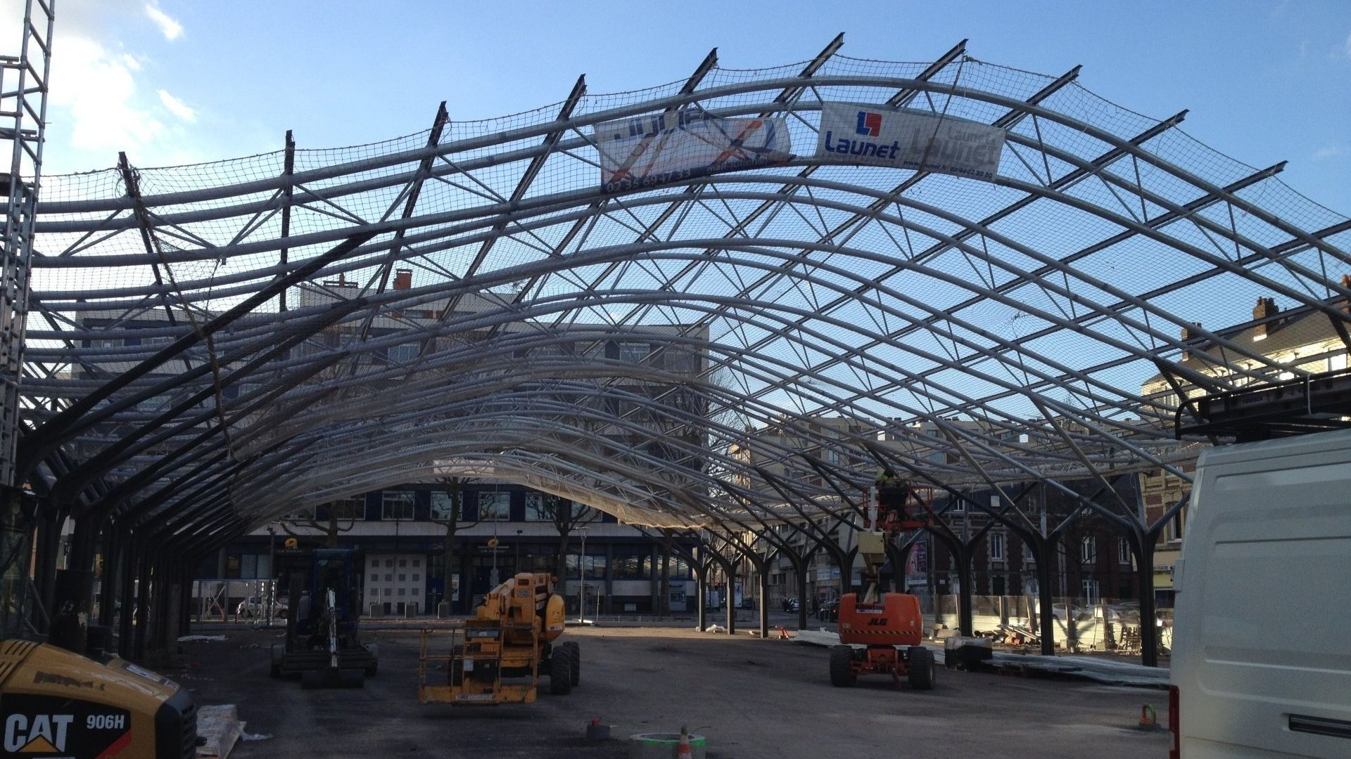 Construction d'une charpente métallique cintrée à l'aide d'engins lourds sur un chantier.